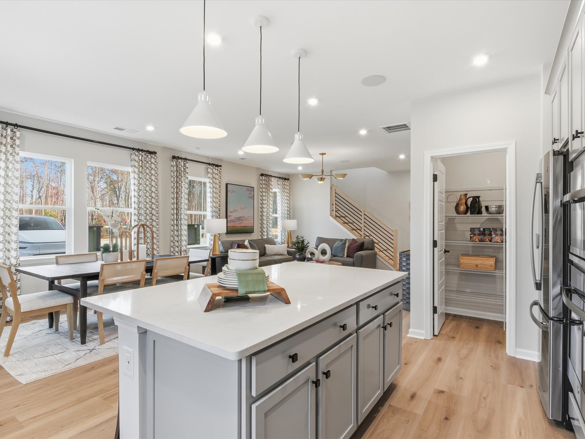 A modern, open-concept kitchen and living area with a large island, pendant lighting, and a mix of wood and neutral tones throughout the space.