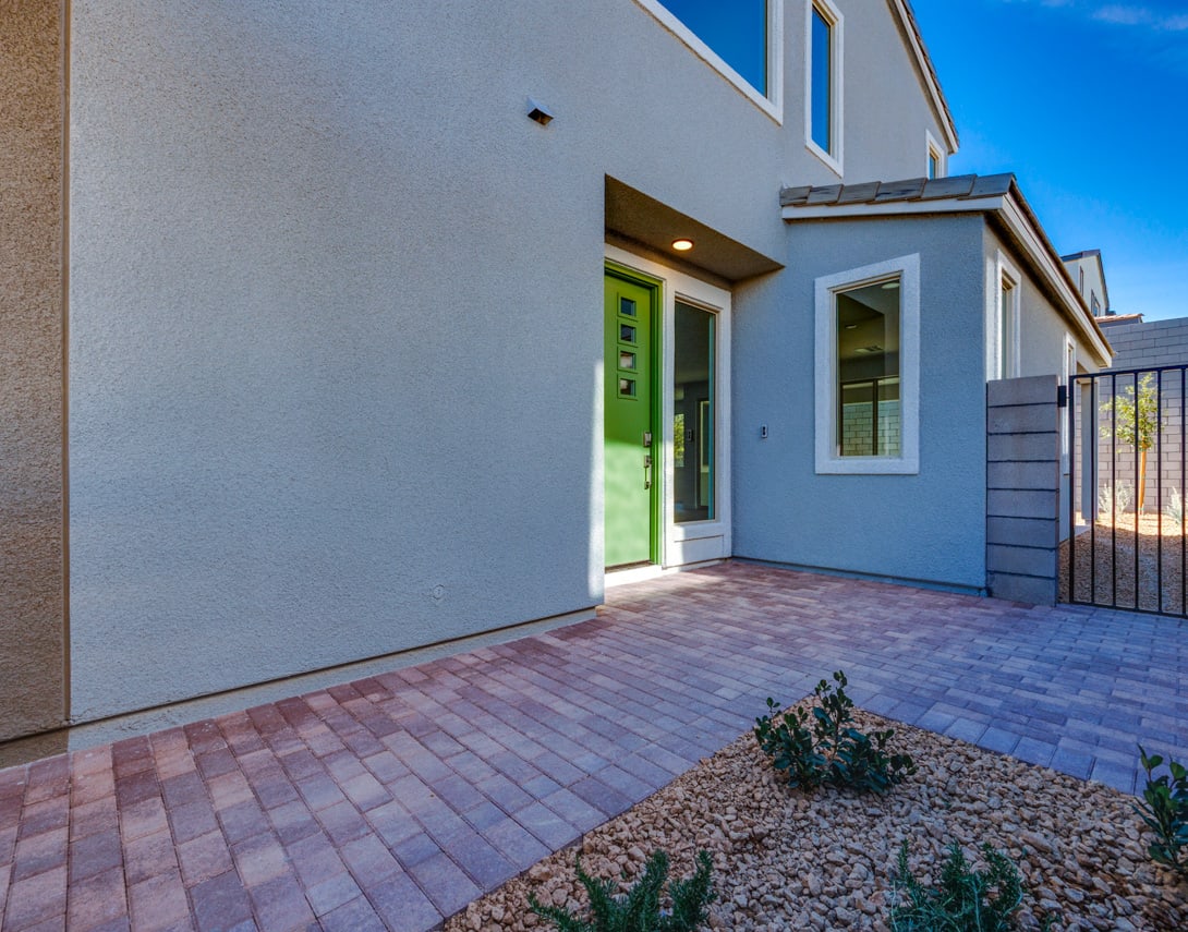 A modern, two-story residential building with a paved entryway, surrounded by landscaping and a clear blue sky in the background.