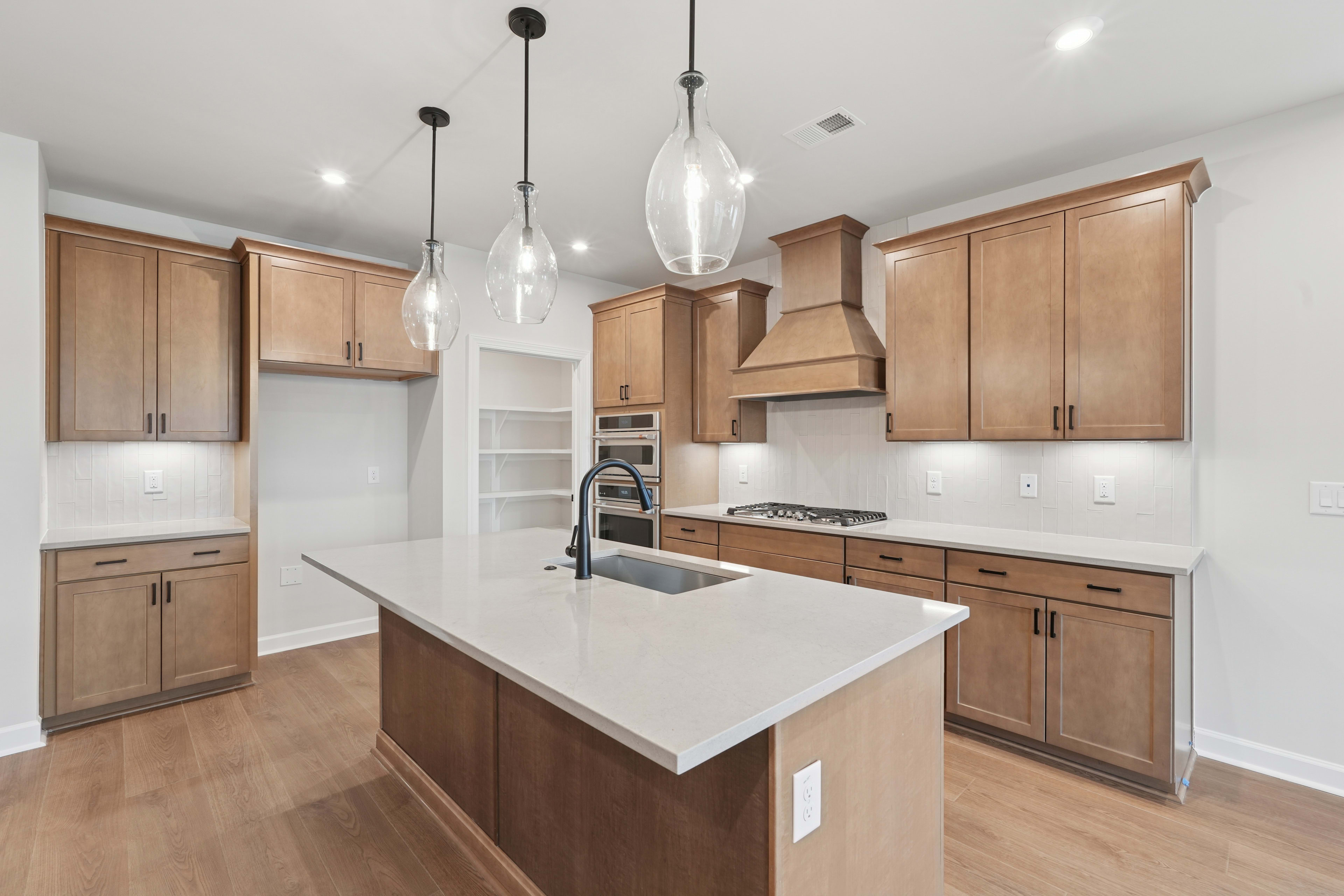 A modern, well-lit kitchen with light wood cabinets, a white countertop, and pendant lights hanging above the central island.