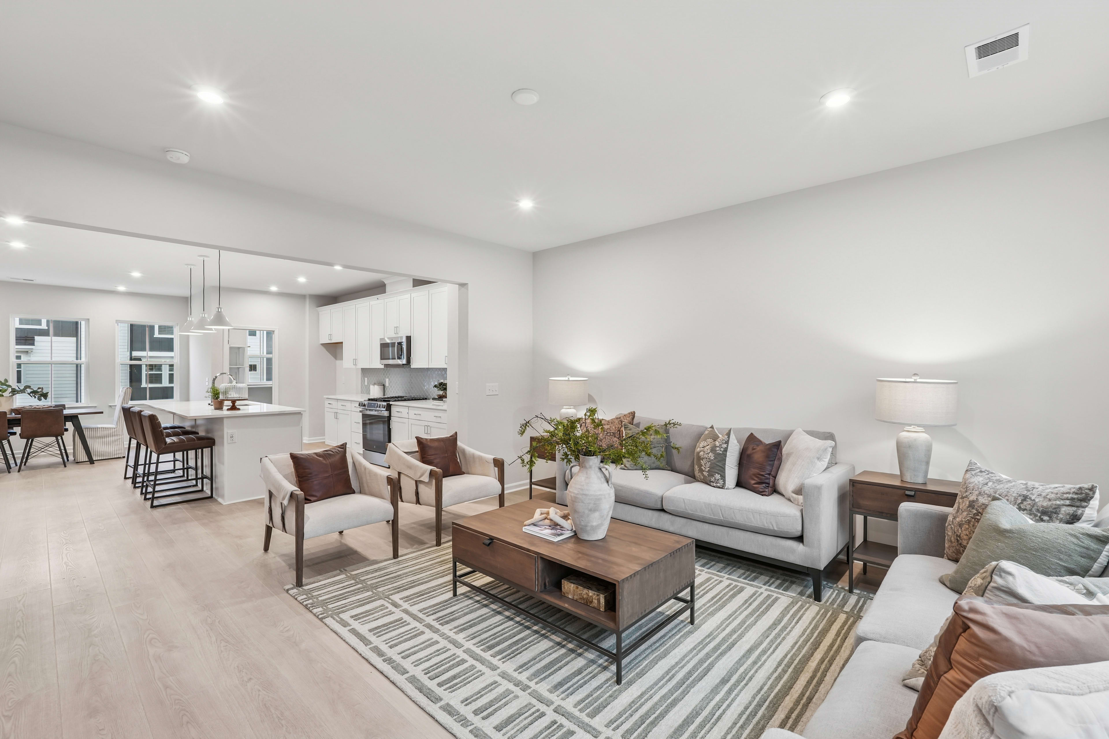 A modern and spacious living room with a gray sofa, wooden coffee table, and patterned rug, along with a kitchen visible in the background.
