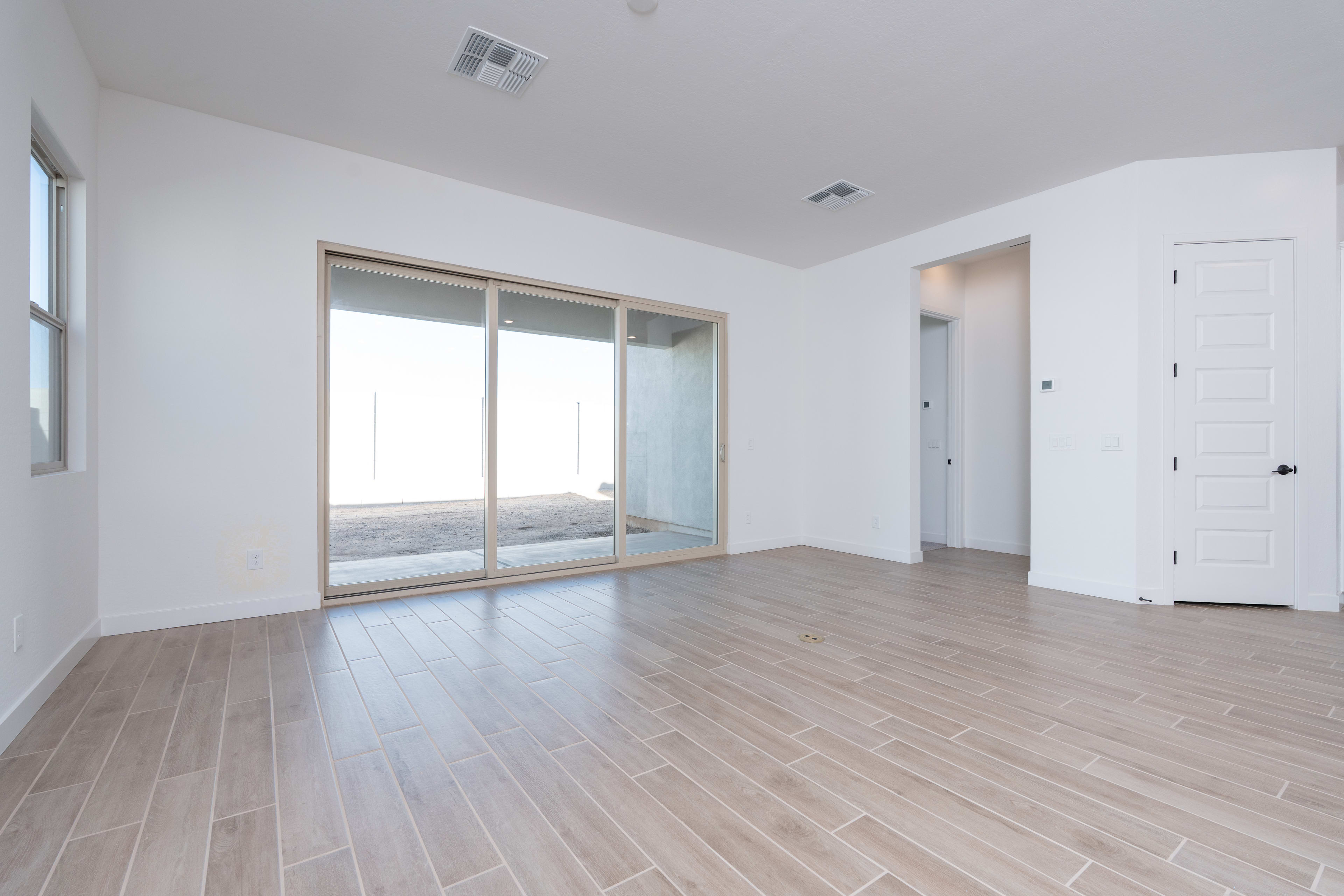 A spacious, minimalist room with large windows, hardwood floors, and a white door leading to another area.