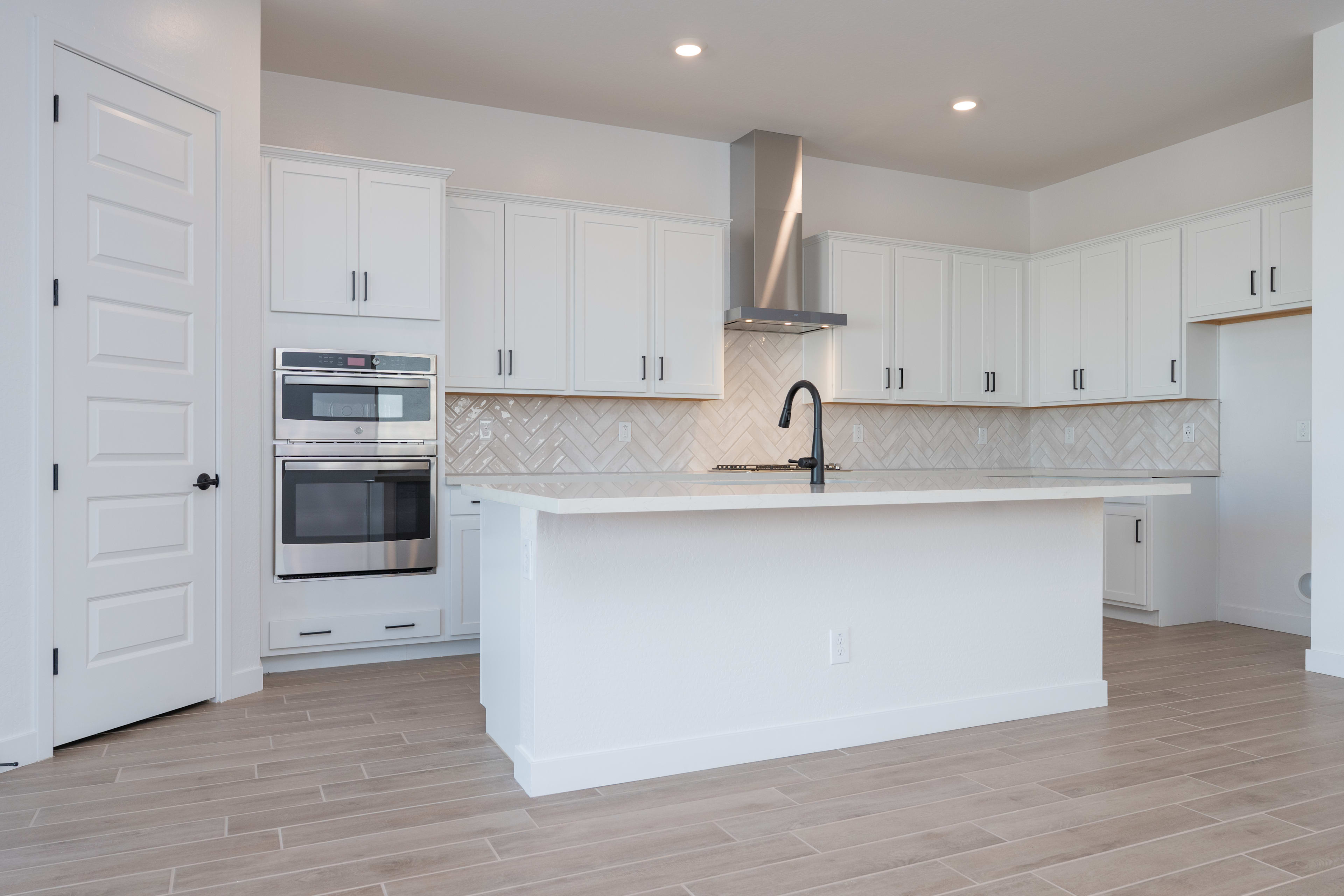 A modern, bright kitchen with white cabinets, stainless steel appliances, and a central island with a sleek black faucet.