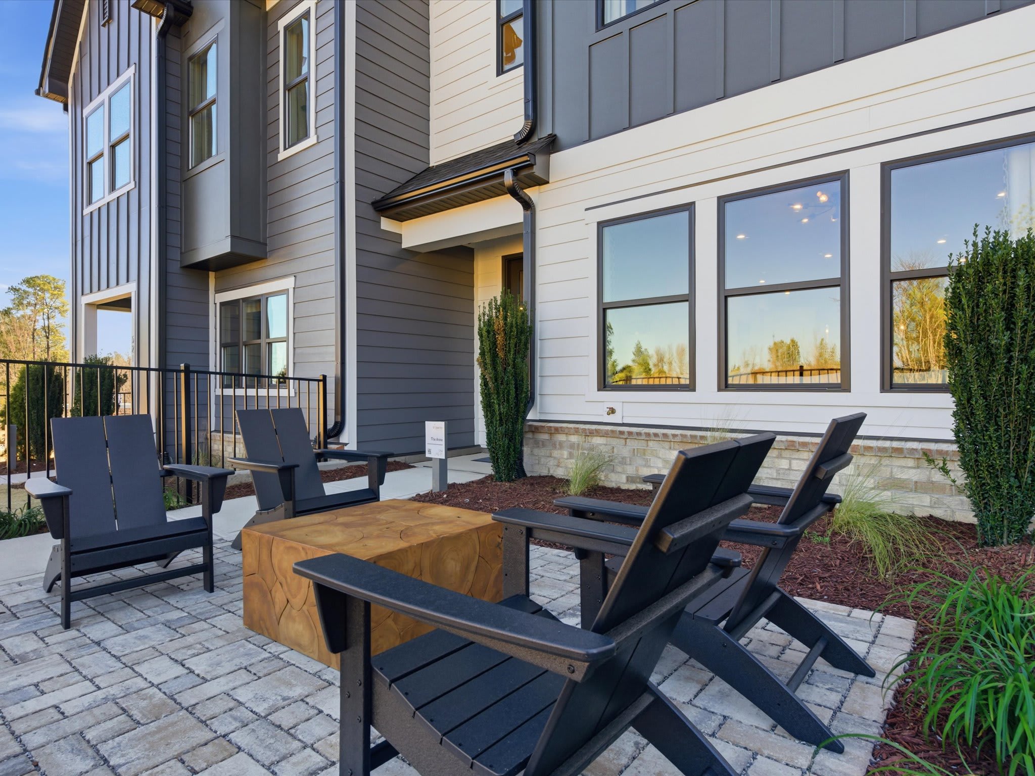 A modern, multi-story residential building with a paved patio area in the foreground, featuring comfortable outdoor furniture and a wooden table.