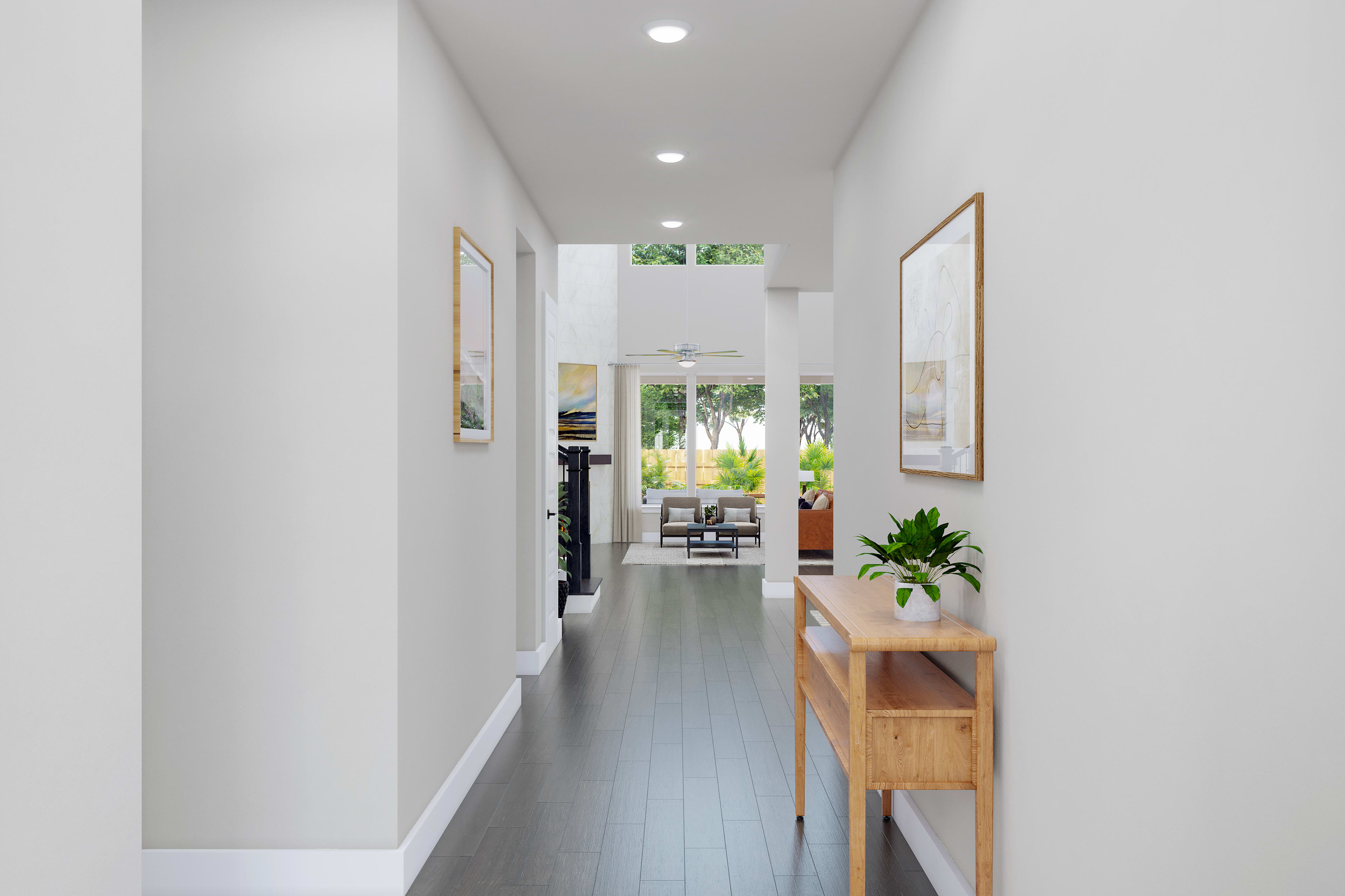 A bright, minimalist hallway with white walls, dark hardwood floors, and a wooden console table in the foreground, leading to a view of the outdoors through a glass door in the background.