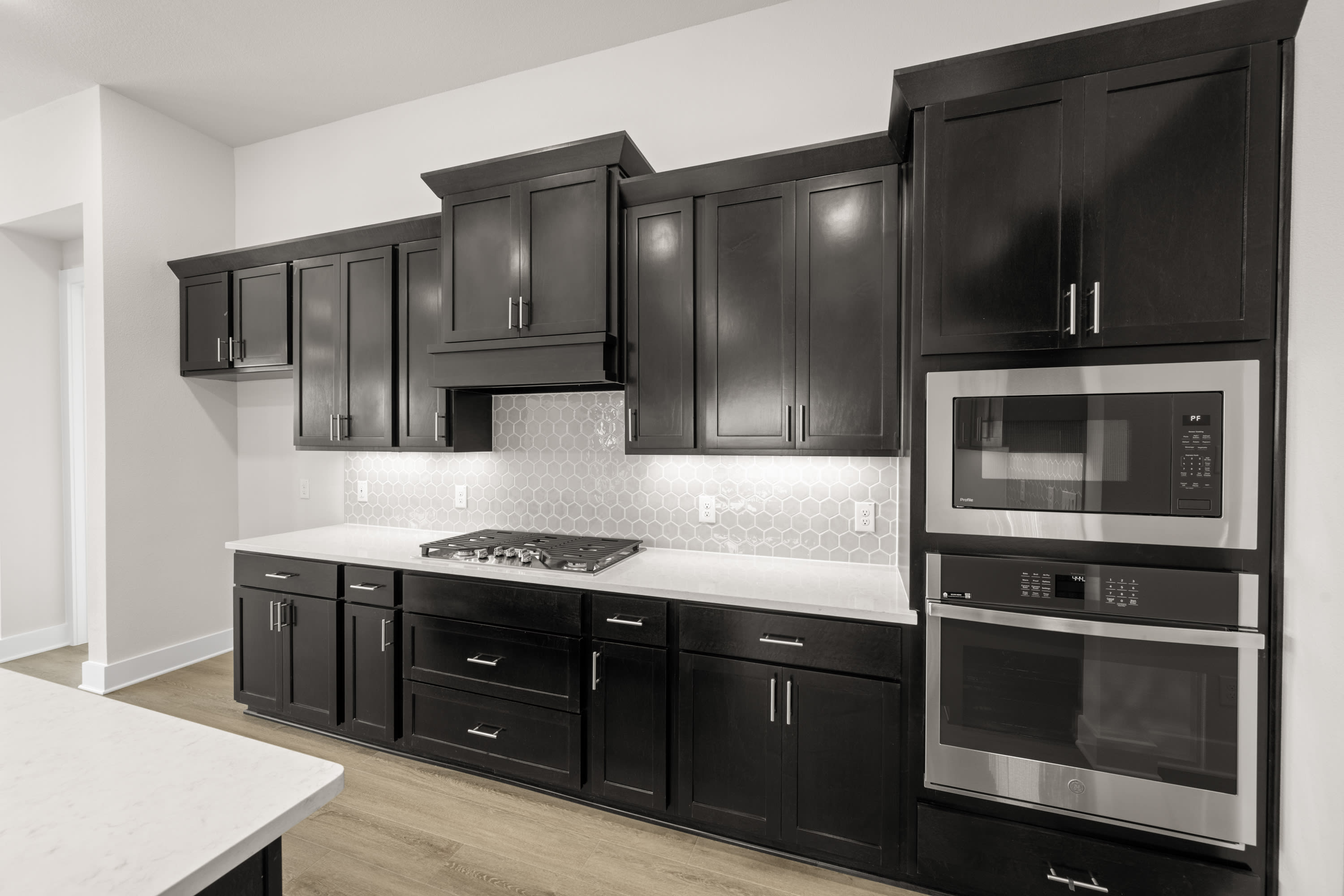 A modern, sleek kitchen with dark wood cabinets, stainless steel appliances, and a white countertop, set against a bright, minimalist background.