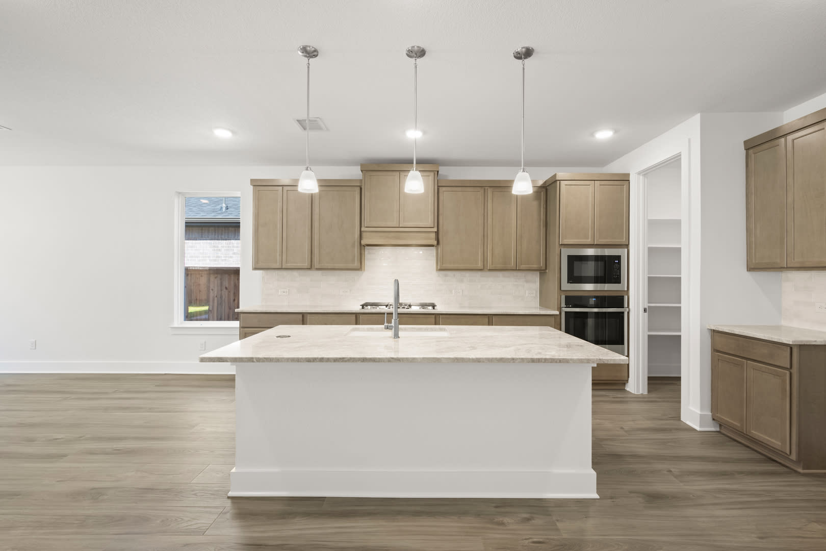 A modern, open-concept kitchen with light-colored wood cabinets, a white island, and pendant lighting fixtures.