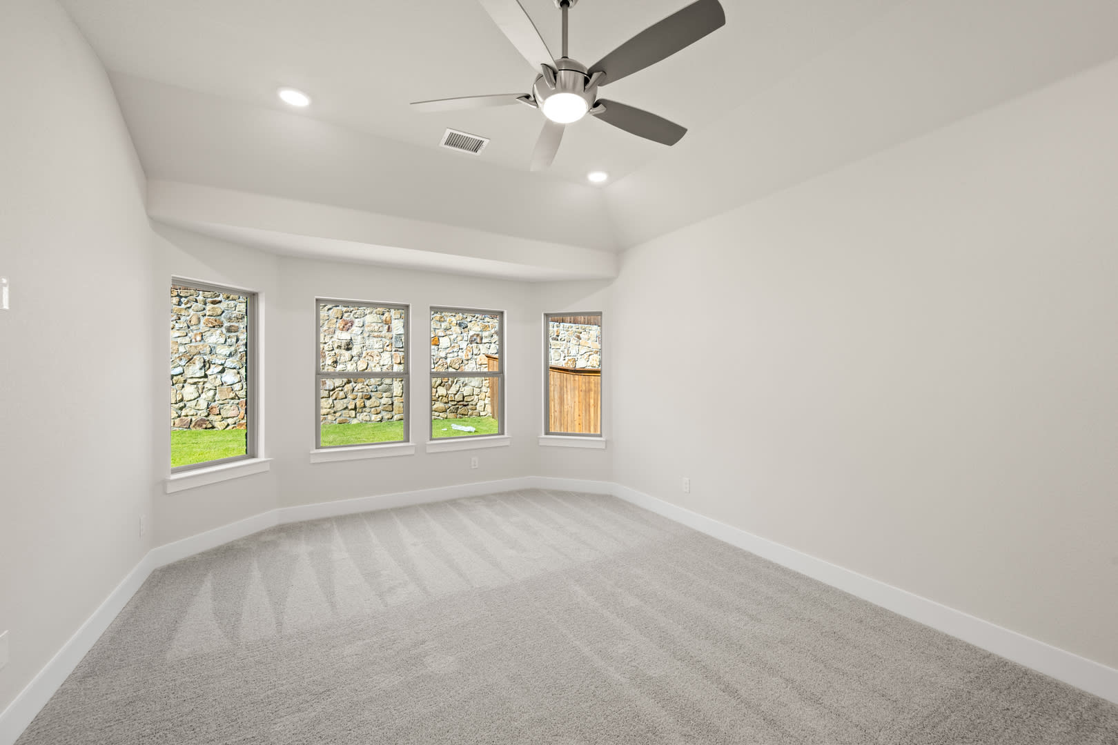 A bright, spacious room with a ceiling fan and large windows overlooking a grassy outdoor area.