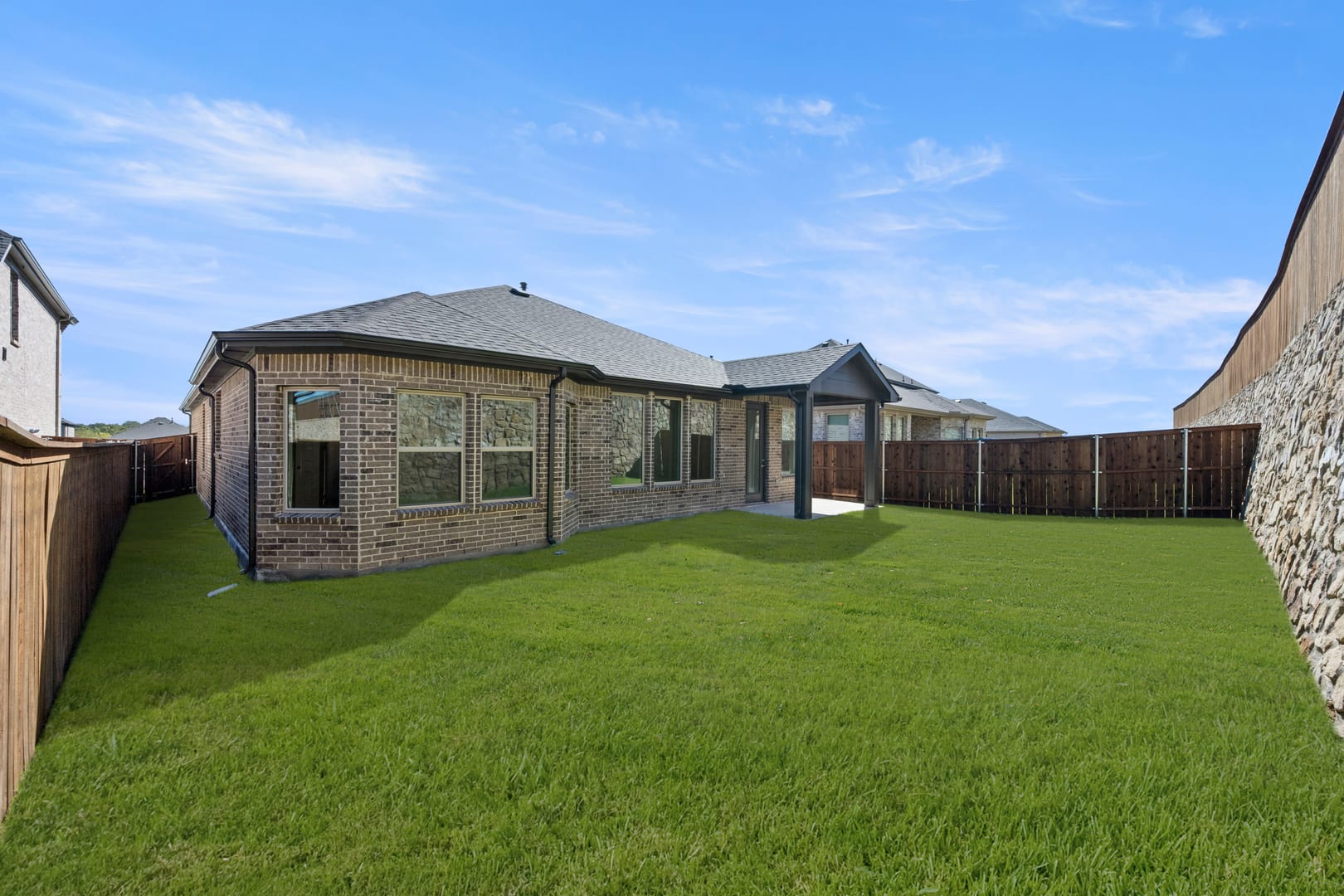 A well-manicured lawn surrounds a brick and siding home with a tiled roof, set against a clear blue sky with wispy clouds.
