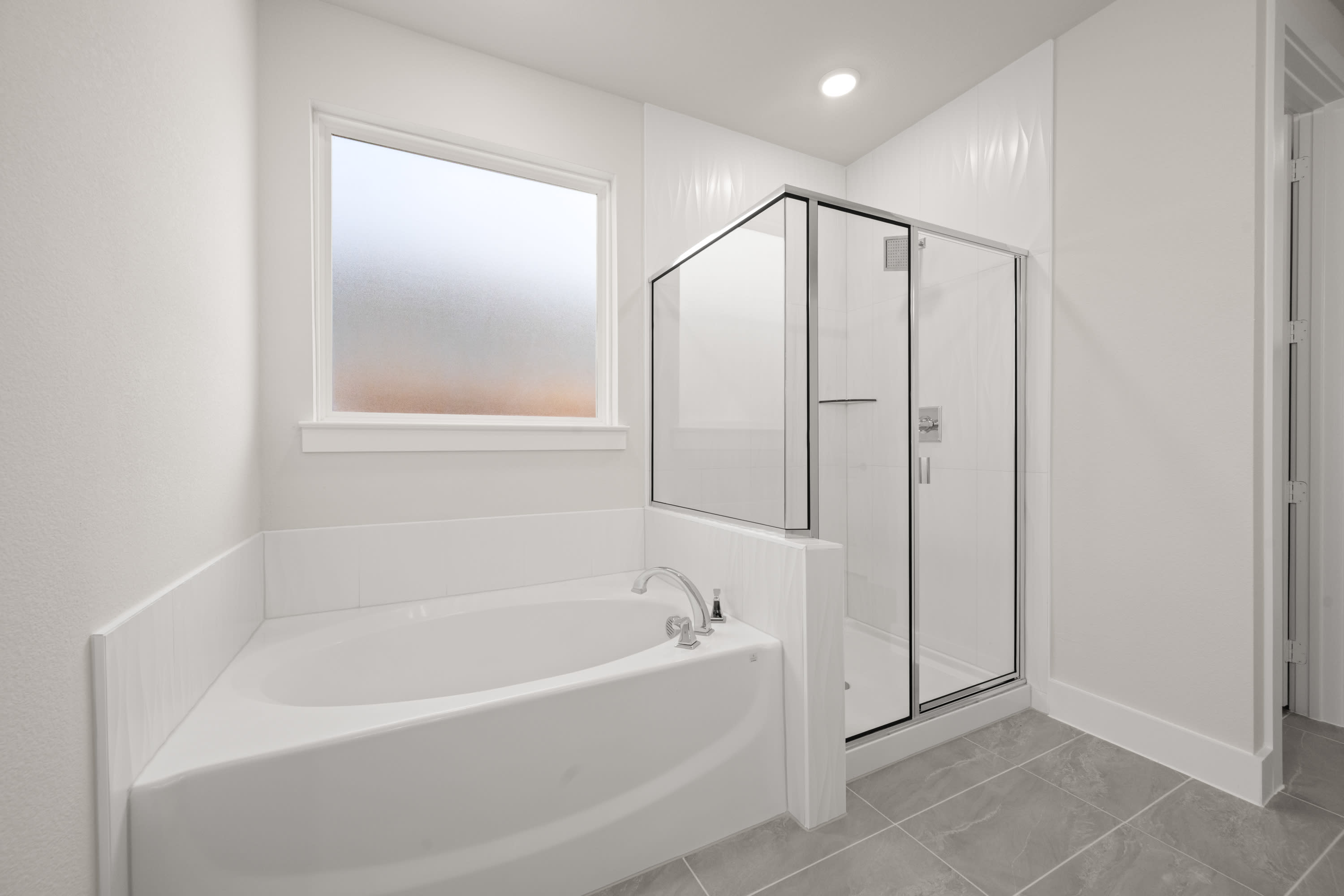 A modern, minimalist bathroom with a freestanding bathtub and a glass-enclosed shower stall, illuminated by a window and recessed lighting.