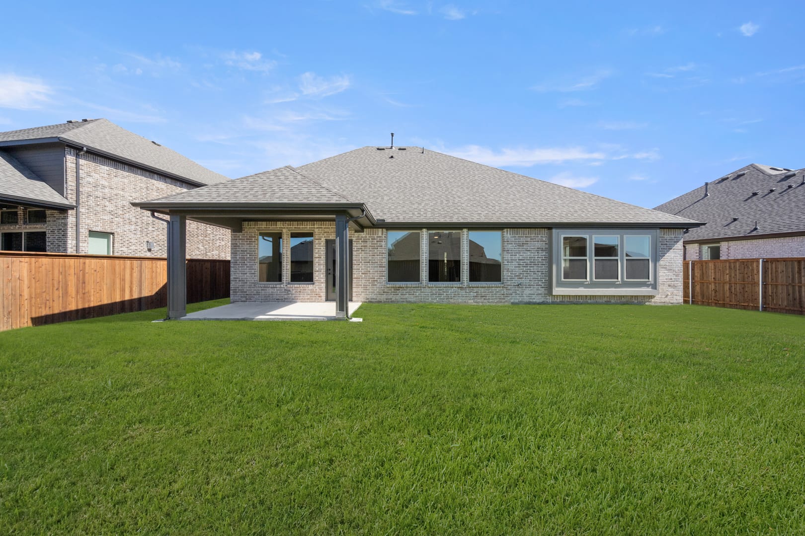 A single-story house with a gray exterior and a large grassy yard in the foreground, set against a clear blue sky.