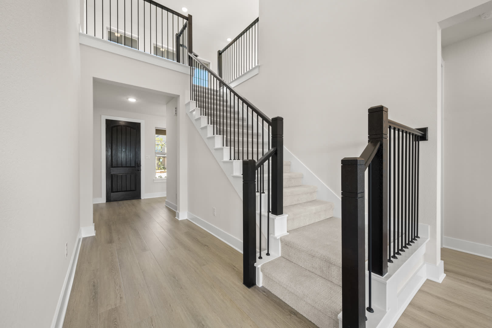 A spacious and modern entryway with a wooden staircase, white walls, and a hardwood floor leading to a doorway.