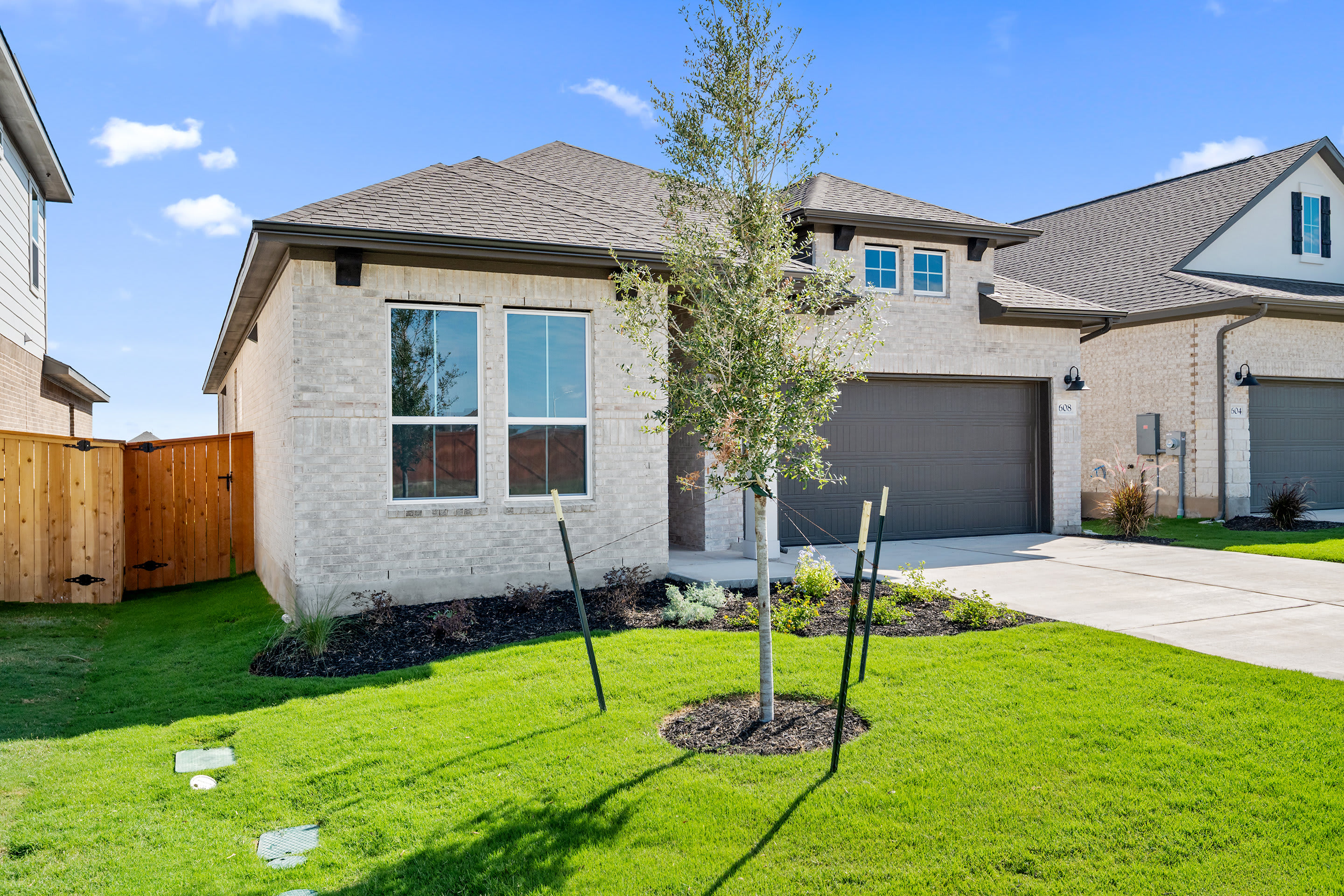 A well-manicured lawn surrounds a modern two-story house with a gray exterior, a tiled roof, and large windows, set against a clear blue sky with scattered clouds.