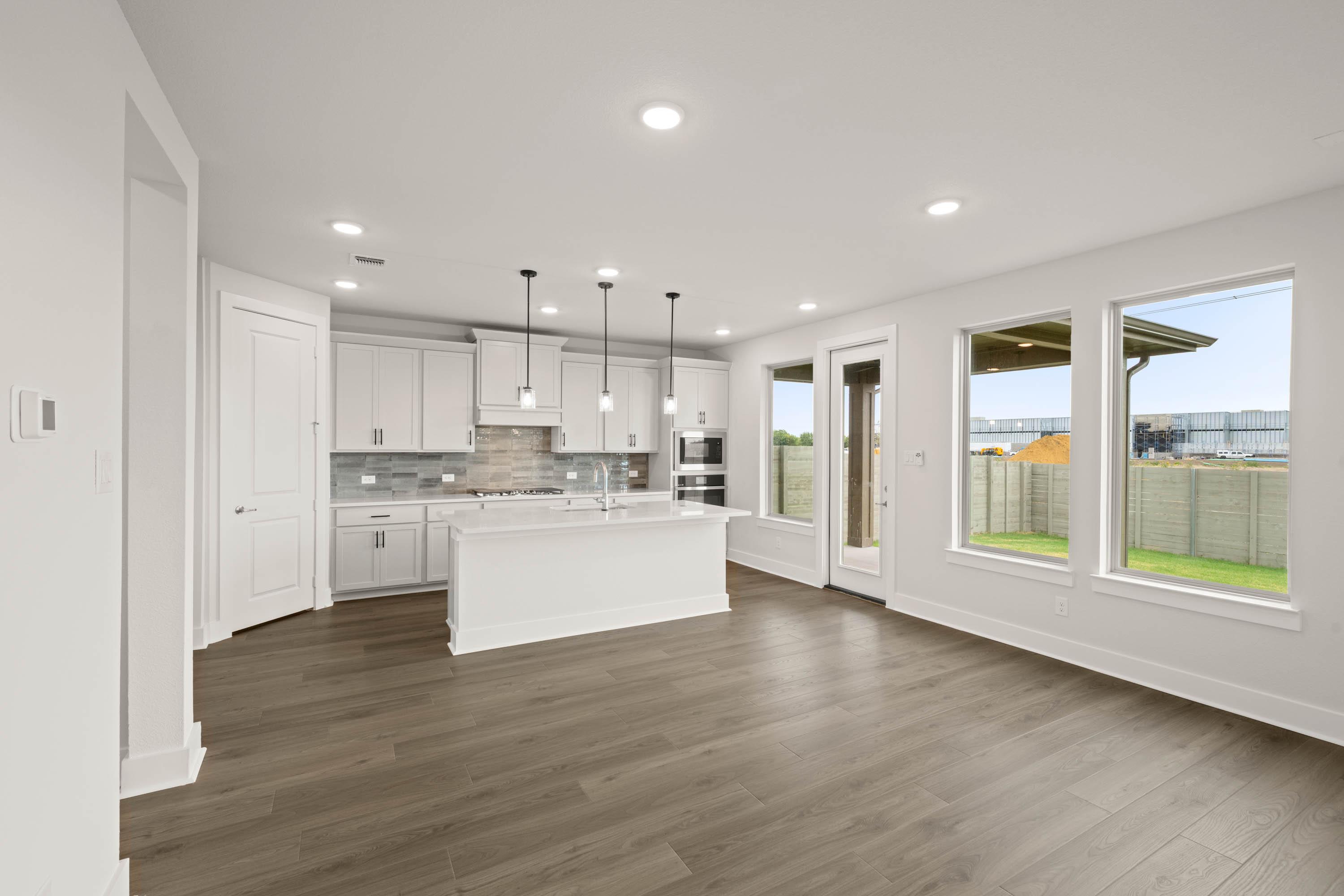 A modern, open-concept kitchen and living space with white cabinets, hardwood floors, and large windows overlooking a backyard.
