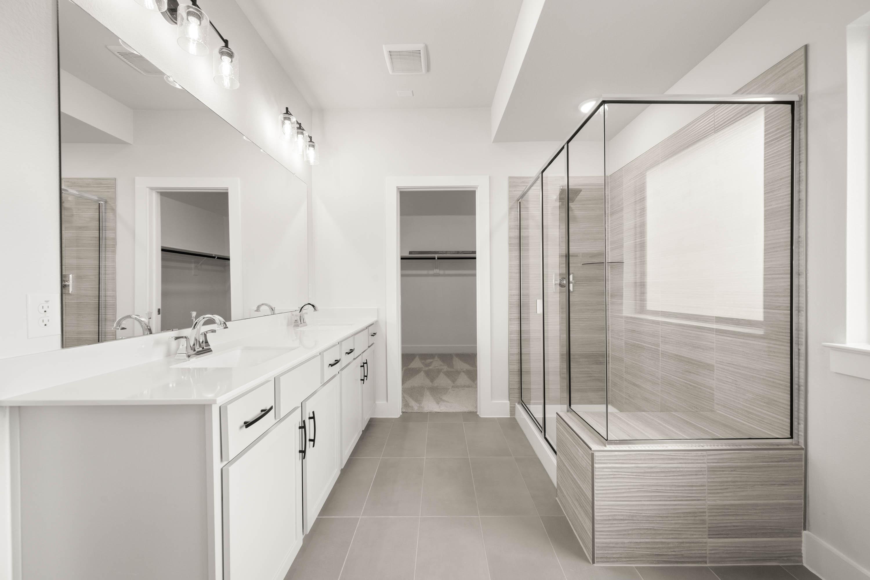 A modern, minimalist bathroom with a white vanity, large mirror, and glass shower enclosure, set against a neutral color palette.