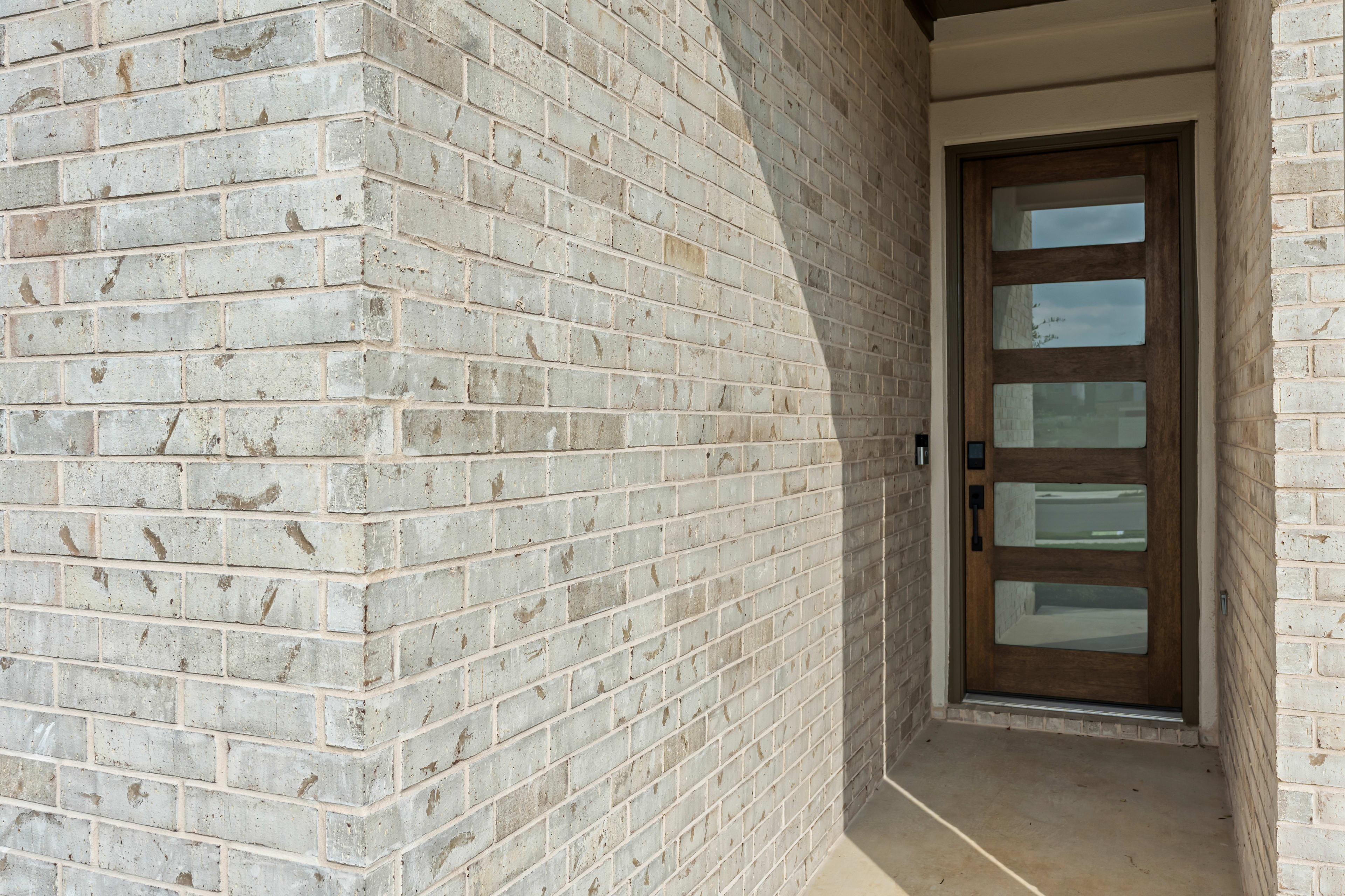The image shows a brick wall with a wooden door and glass panels, leading to an interior space.