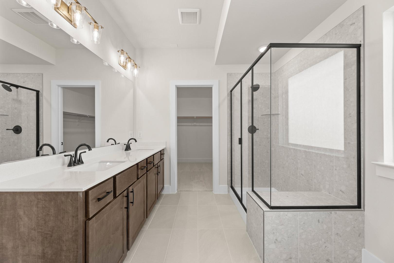 A modern and spacious bathroom with a double vanity, a large glass-enclosed shower, and recessed lighting fixtures on the ceiling.