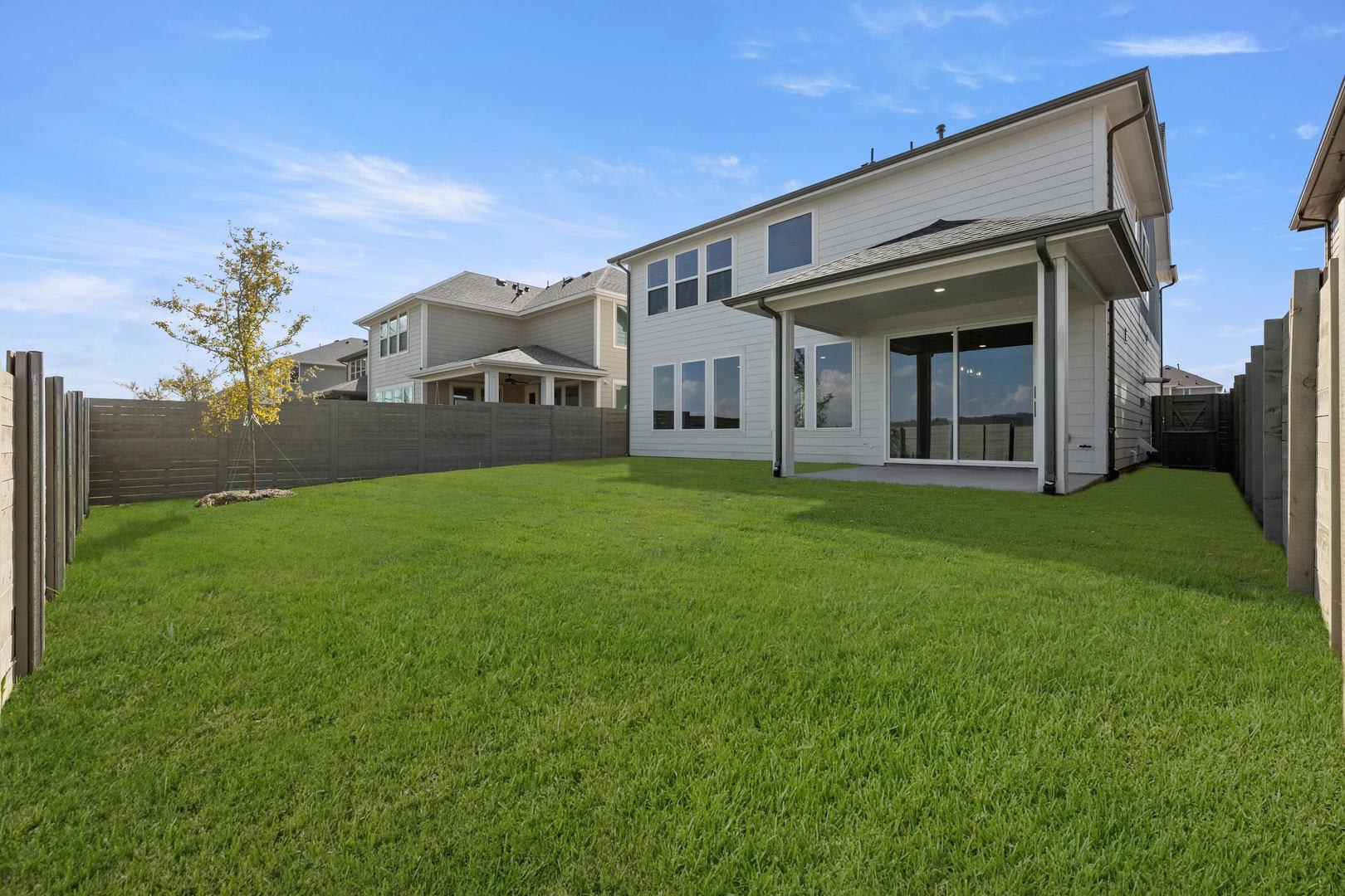 A well-manicured lawn in the foreground leads to a modern, two-story residential building with large windows and a covered patio in the background.