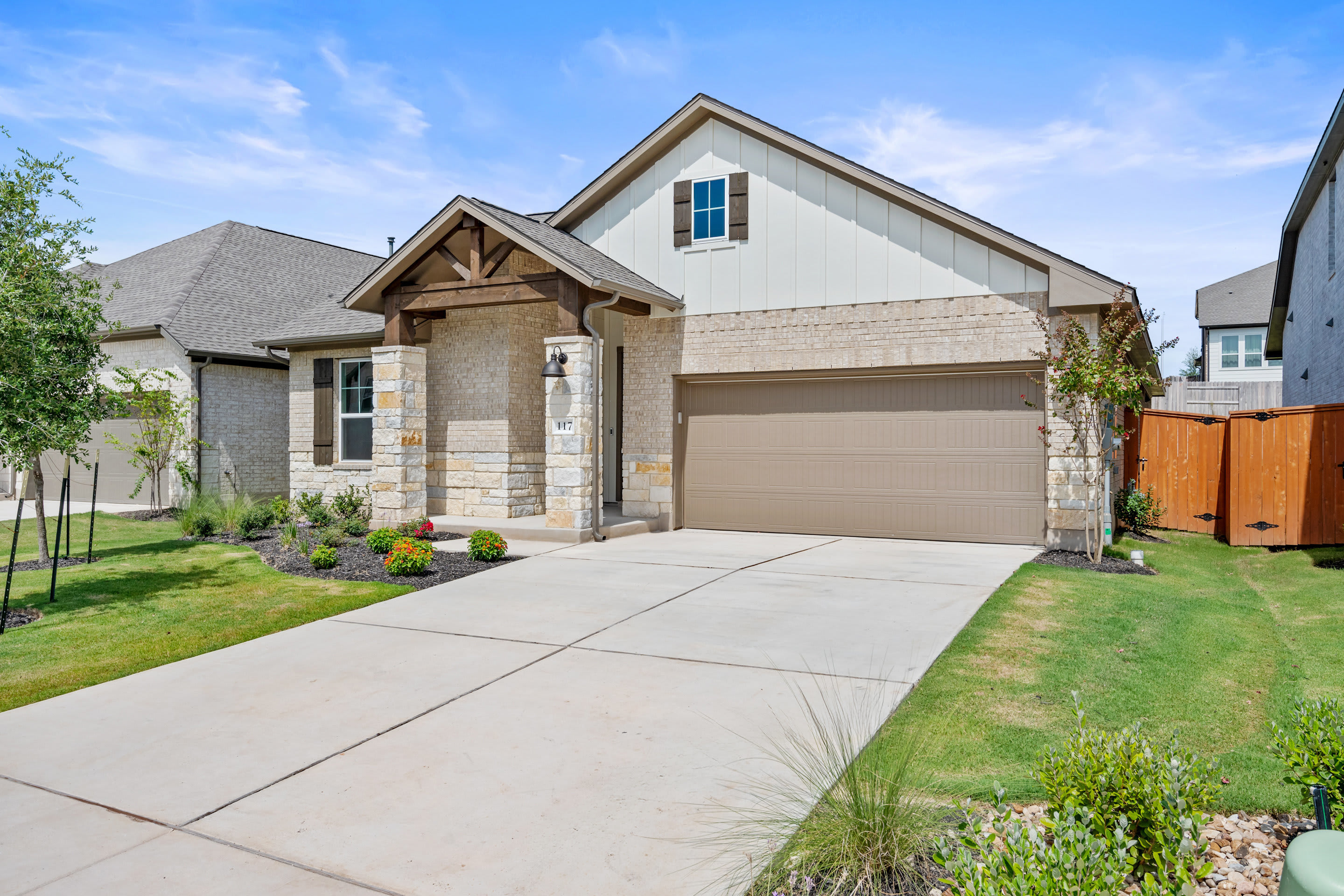 A well-maintained single-story house with a garage, surrounded by a neatly landscaped yard and a paved driveway, set against a clear blue sky.