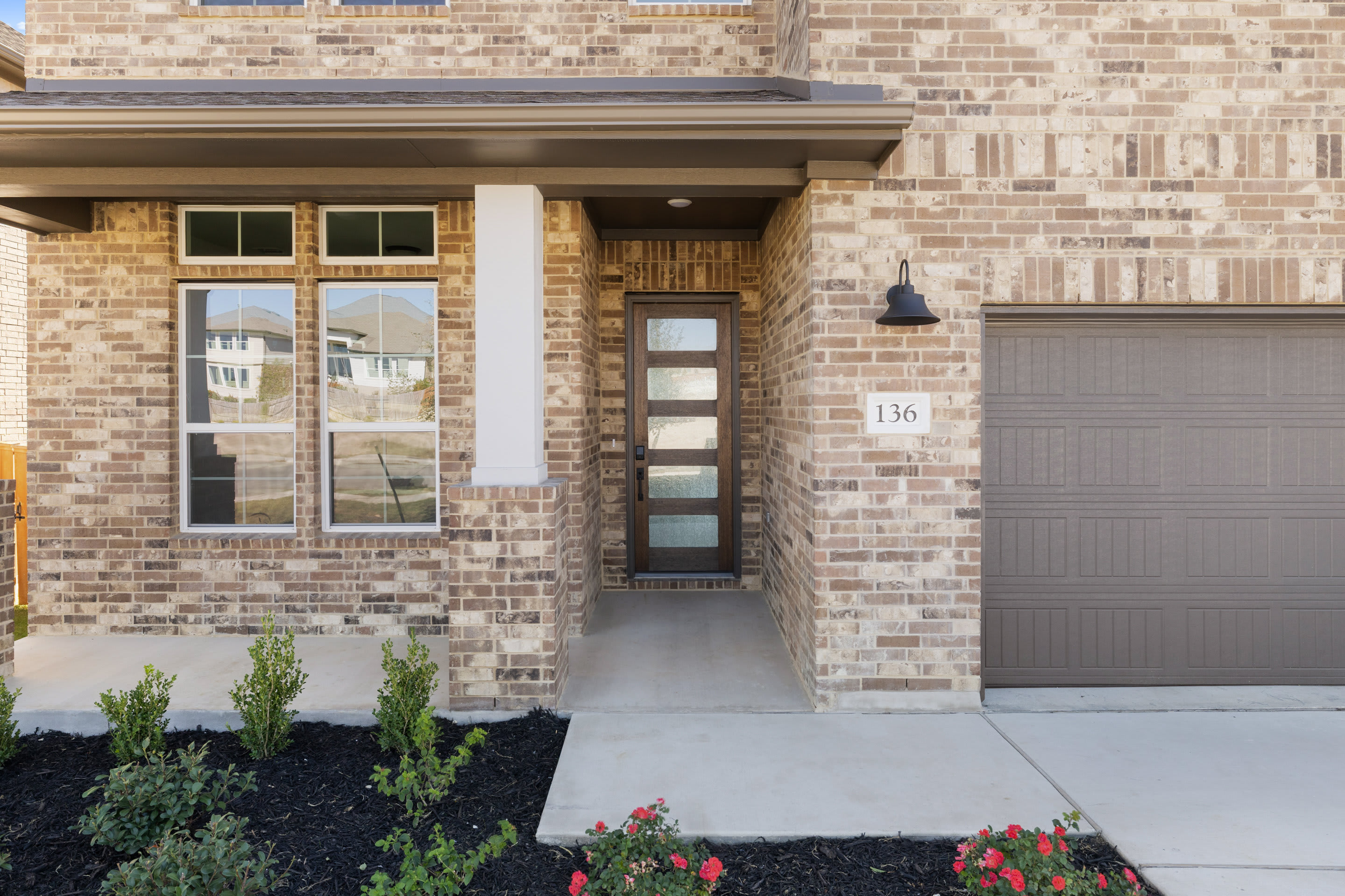 A modern brick house with a covered entryway, a garage door, and landscaping in the foreground.