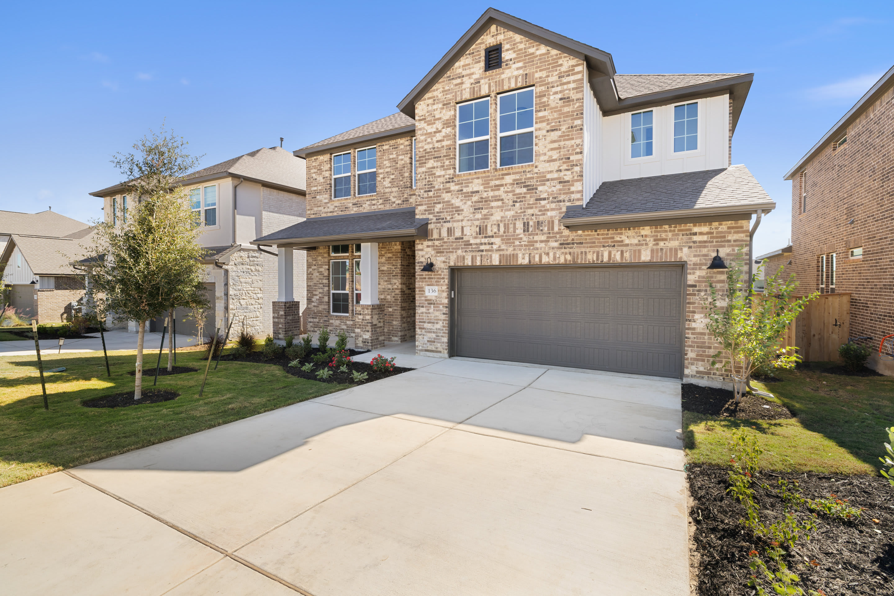 A two-story stone and siding house with a garage, surrounded by a well-manicured lawn and landscaping, set against a clear blue sky.