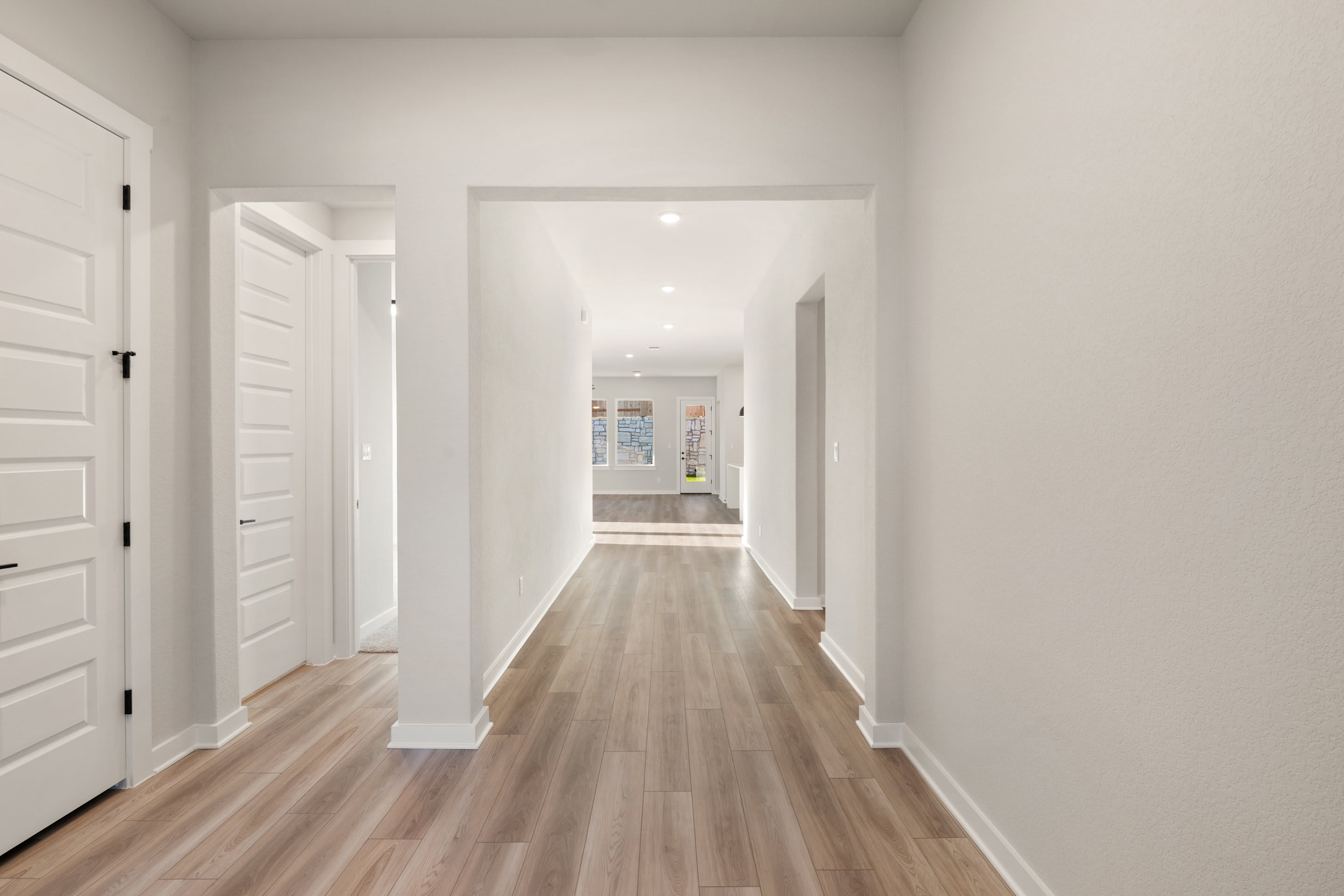A bright, spacious hallway with white walls and a wooden floor extends into the distance, leading to additional rooms.