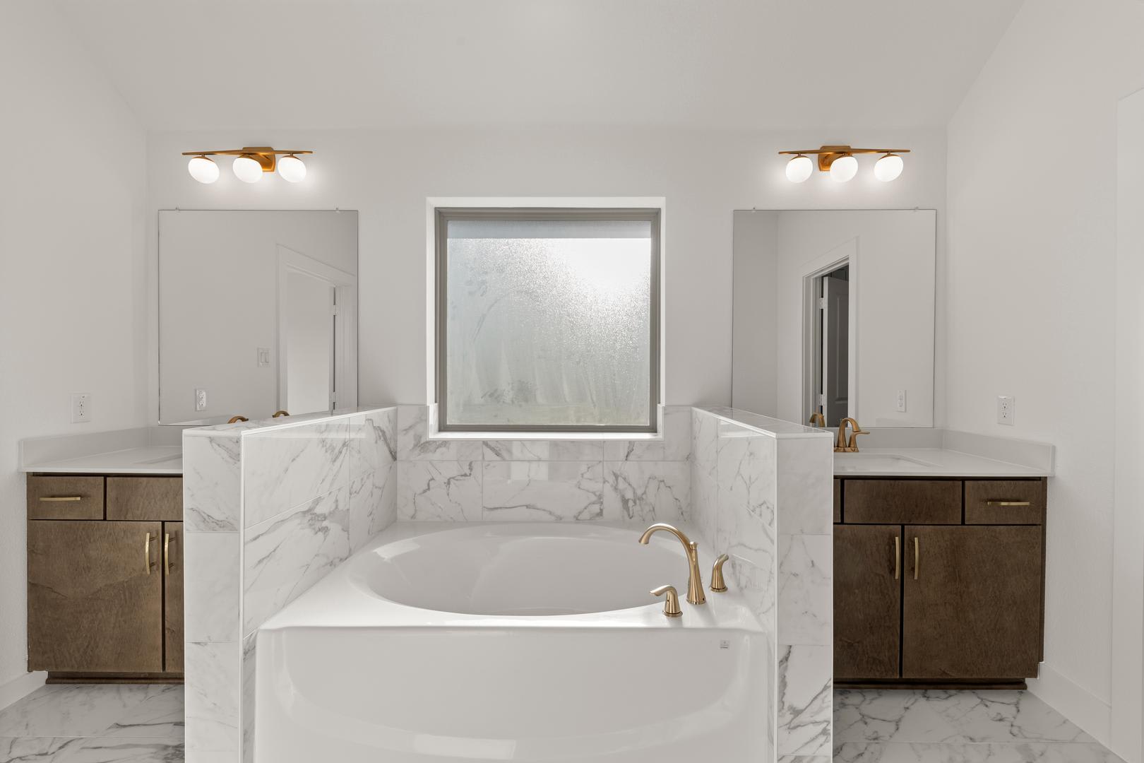 A modern and elegant bathroom with a white marble-like vanity, a freestanding bathtub, and two wall-mounted mirrors with lighting fixtures.