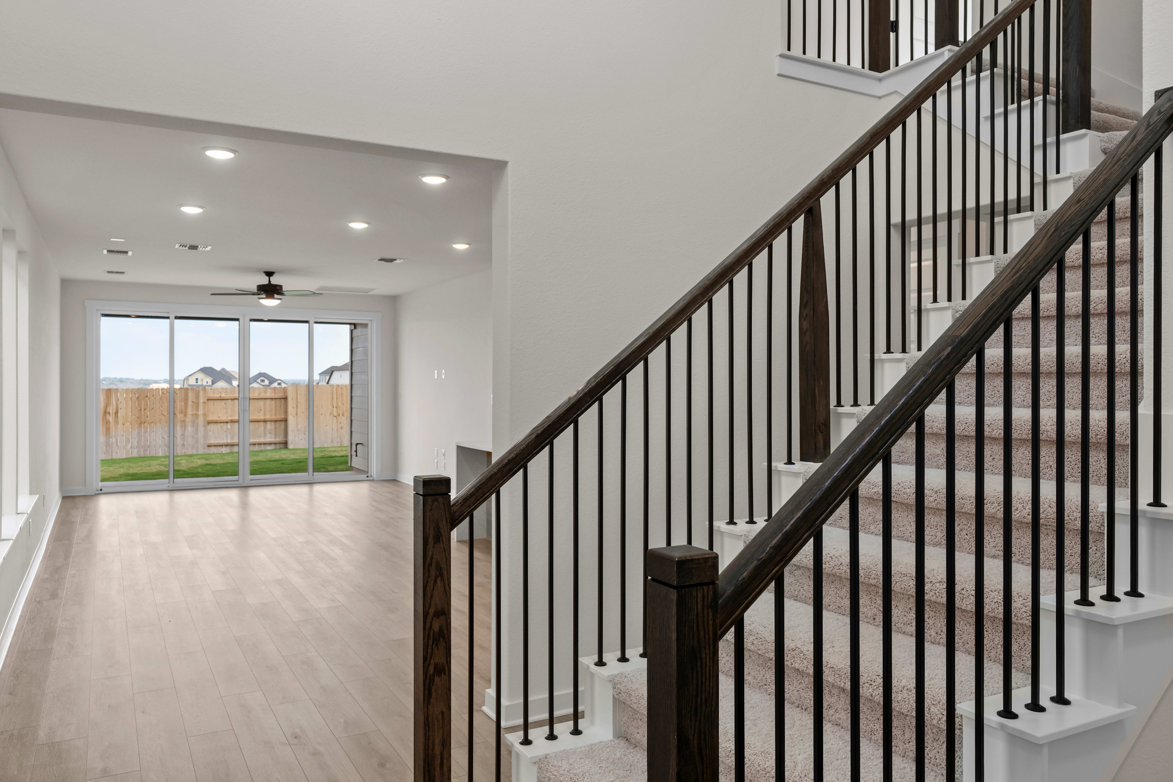 A modern, open-concept interior with a wooden staircase and metal railing leading to a bright, airy space with a view of a fenced backyard.