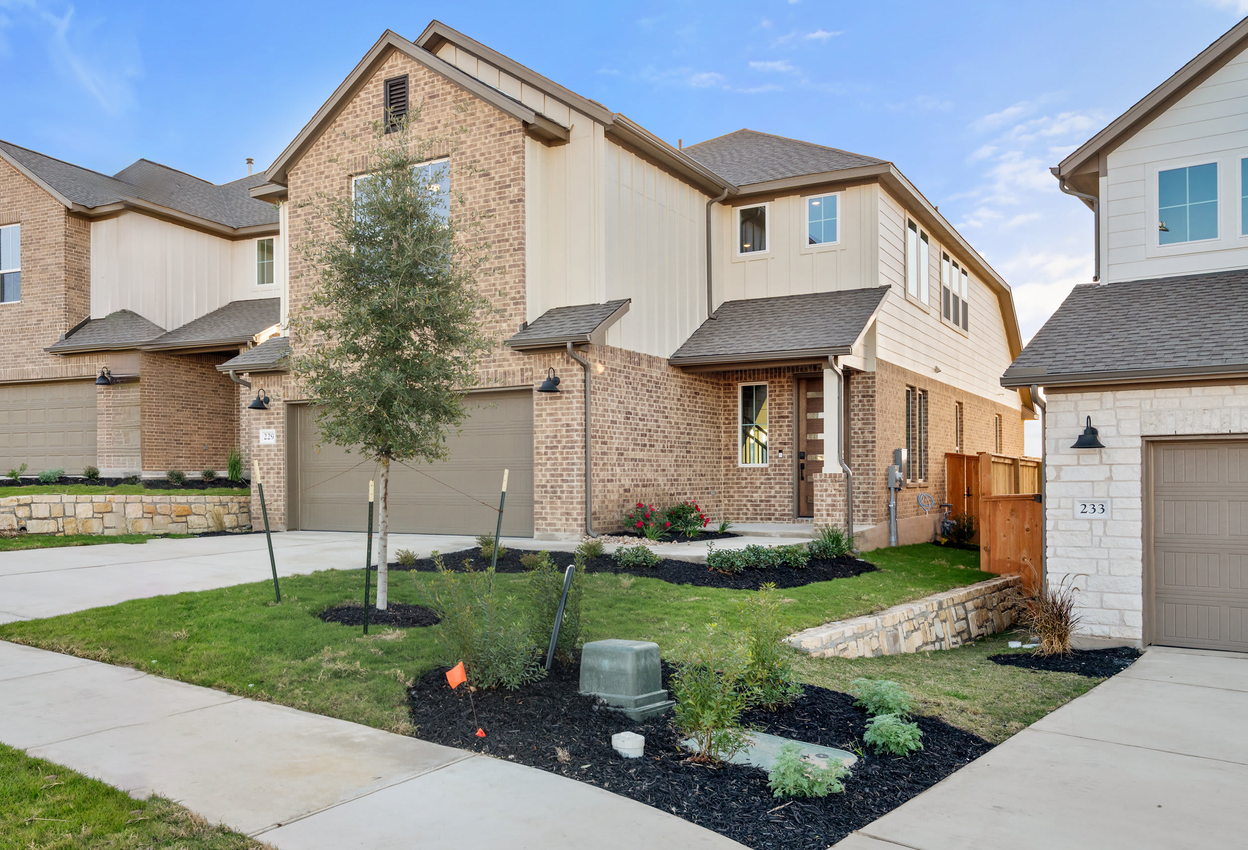 A two-story brick and stucco townhouse with a well-manicured front yard, surrounded by other similar homes in a residential neighborhood.