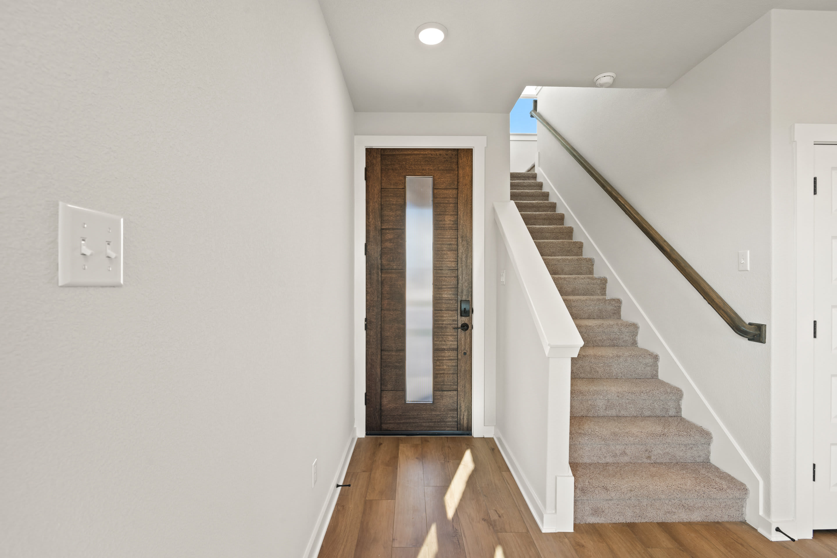 A bright and airy interior with a wooden door, a staircase leading upstairs, and a clean, minimalist design.