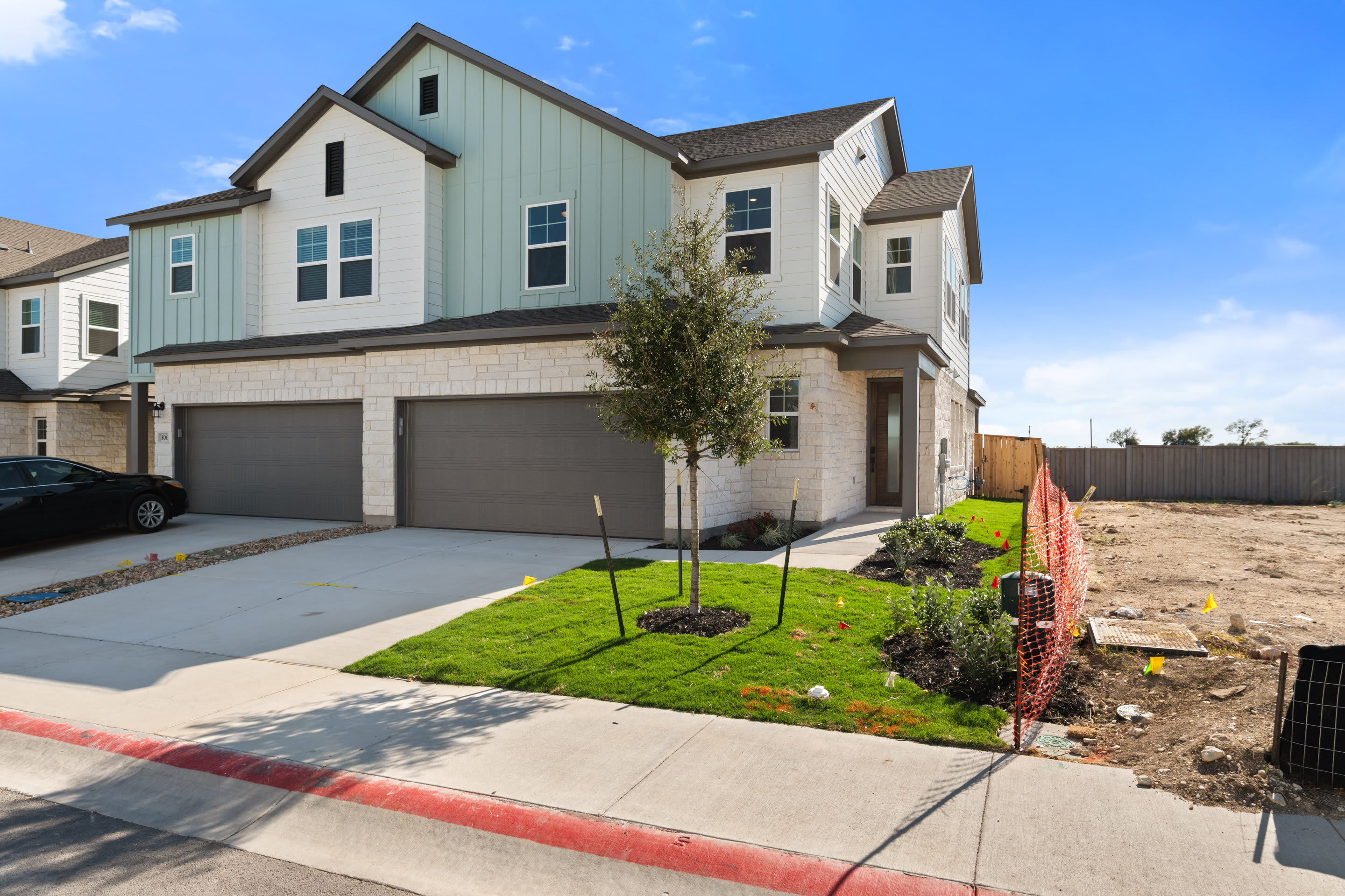 A modern two-story house with a garage, surrounded by a well-manicured lawn and landscaping, stands against a clear blue sky.
