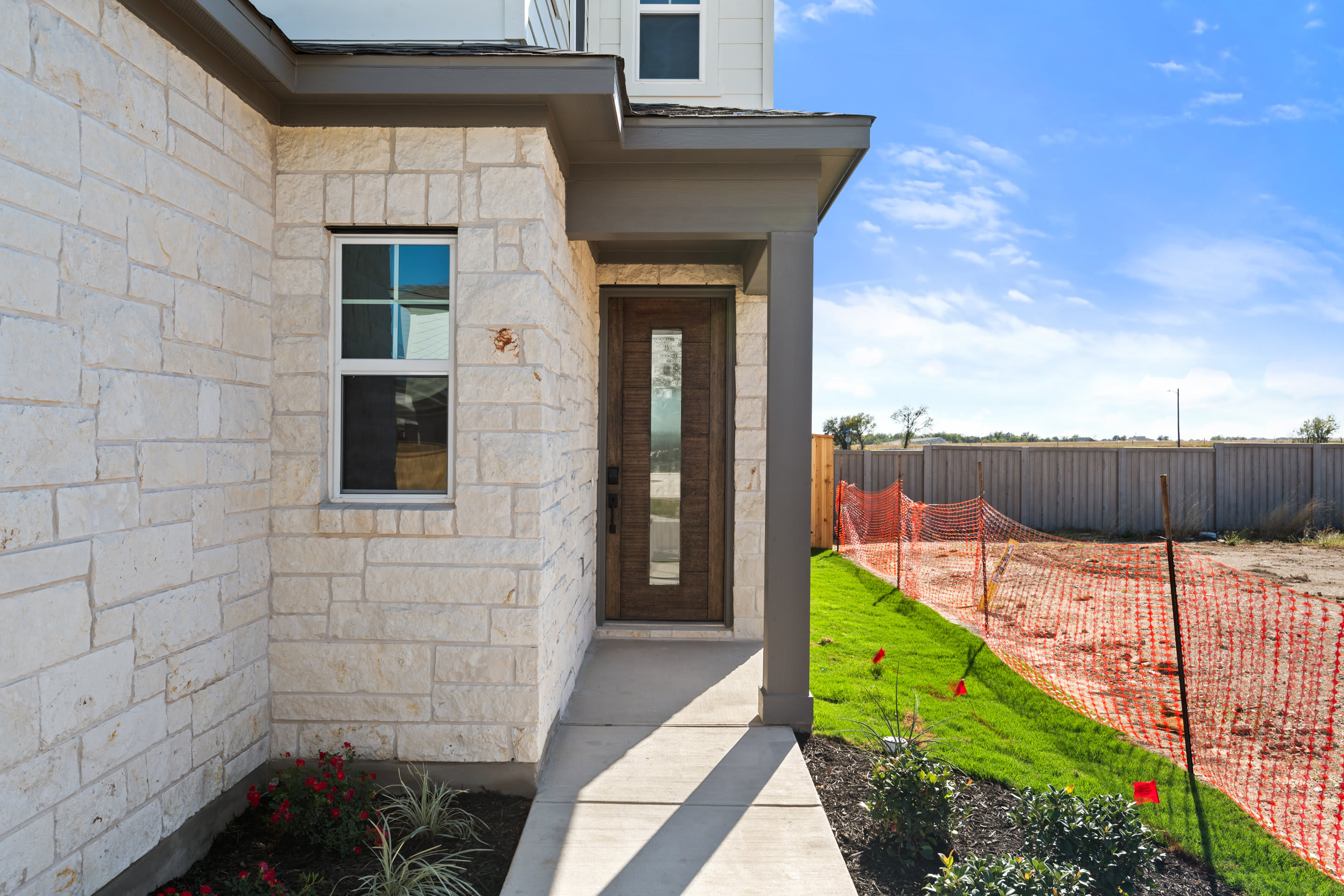 A modern, two-story residential building with a stone exterior, surrounded by a well-manicured lawn and a wooden fence in the background.