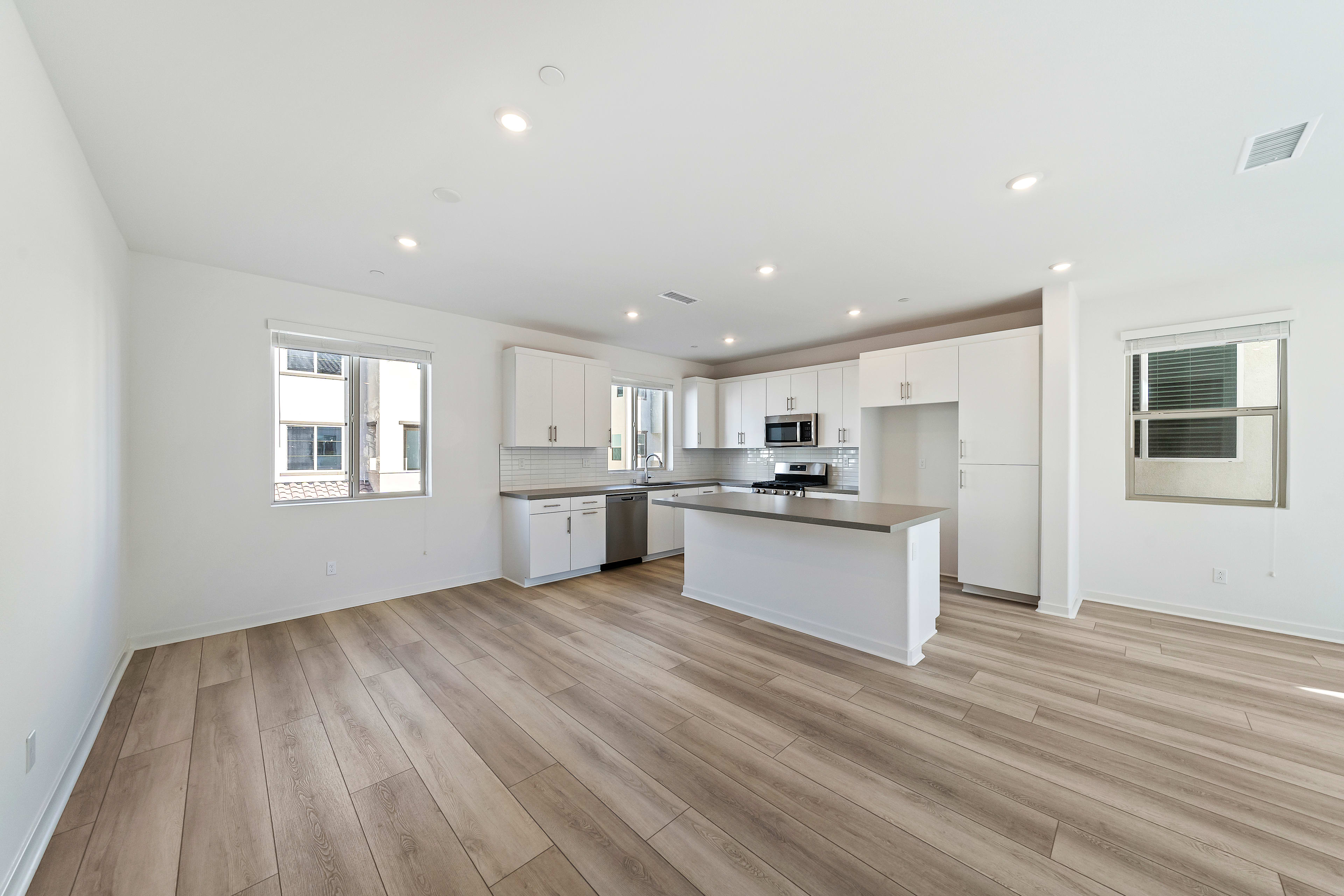 A modern, open-concept kitchen with white cabinets, stainless steel appliances, and a hardwood floor that extends throughout the room.