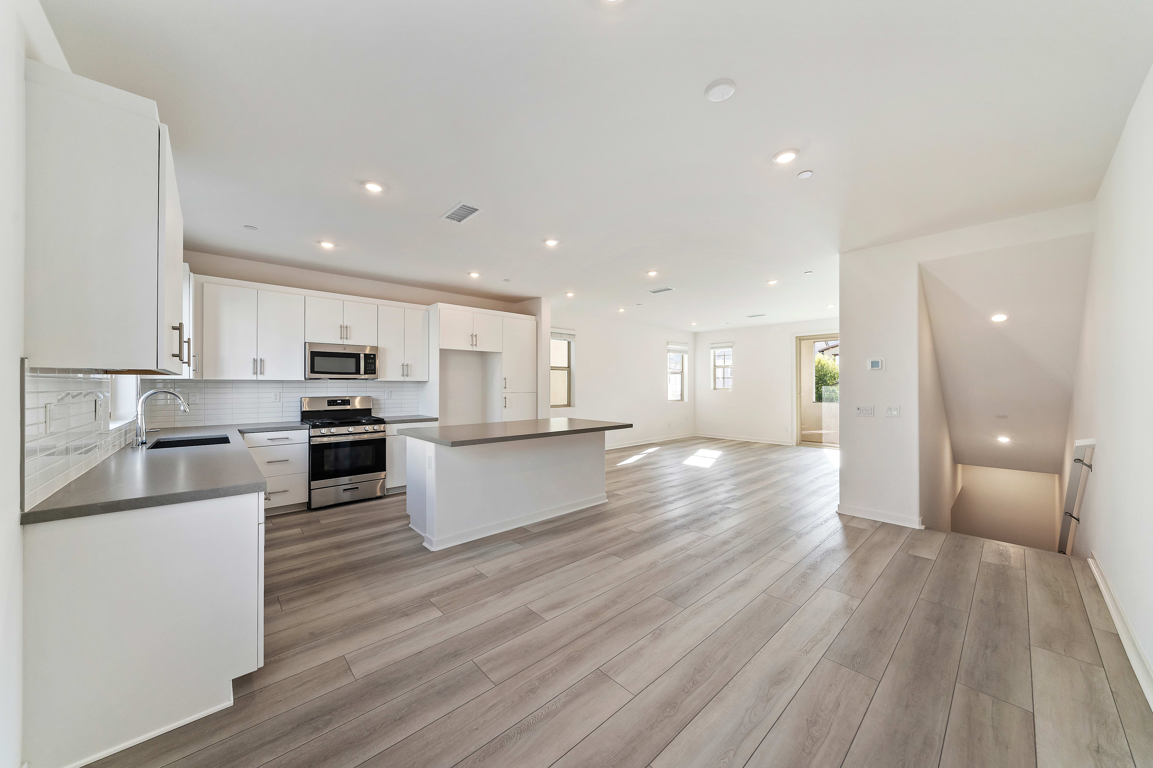 A modern, open-concept kitchen and living space with white cabinets, stainless steel appliances, and a hardwood floor that extends throughout the room.