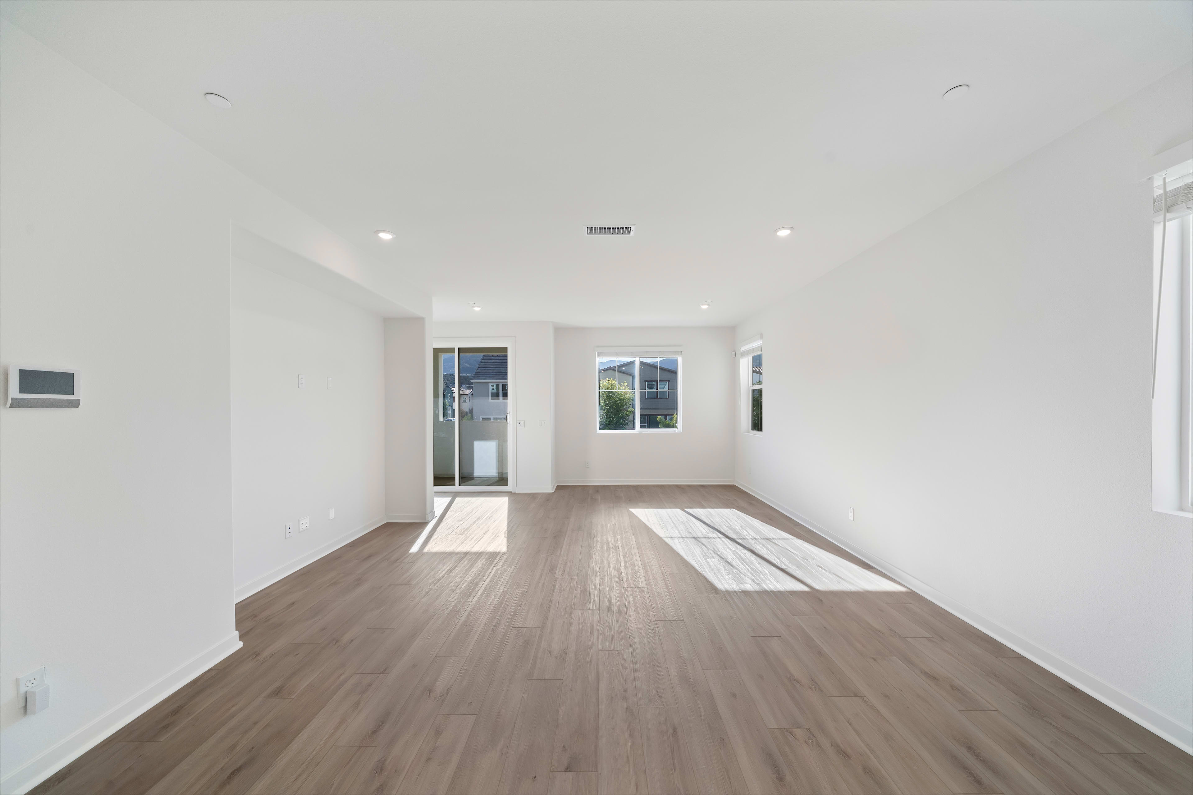 A spacious, well-lit room with a hardwood floor and a large window overlooking an outdoor scene.