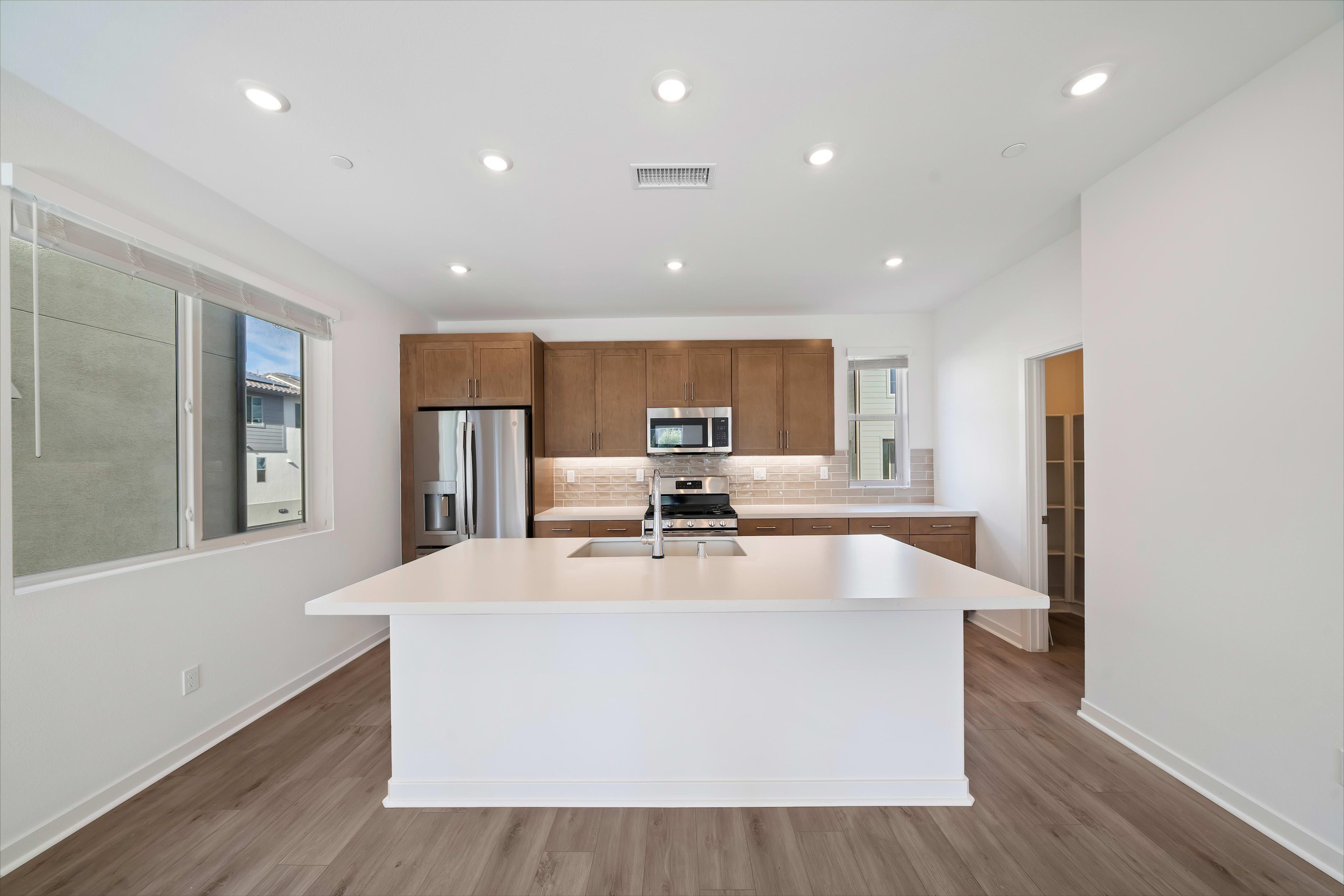 A modern, open-concept kitchen with white countertops, wooden cabinets, and stainless steel appliances, set against a bright, airy background.