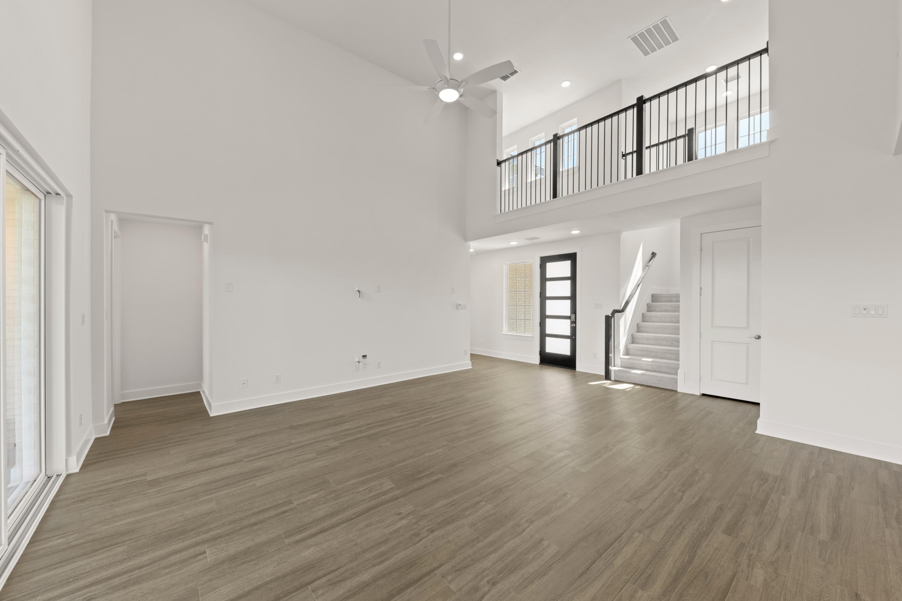 A spacious, open-concept living area with a high ceiling, hardwood flooring, and a staircase leading to an upper level.