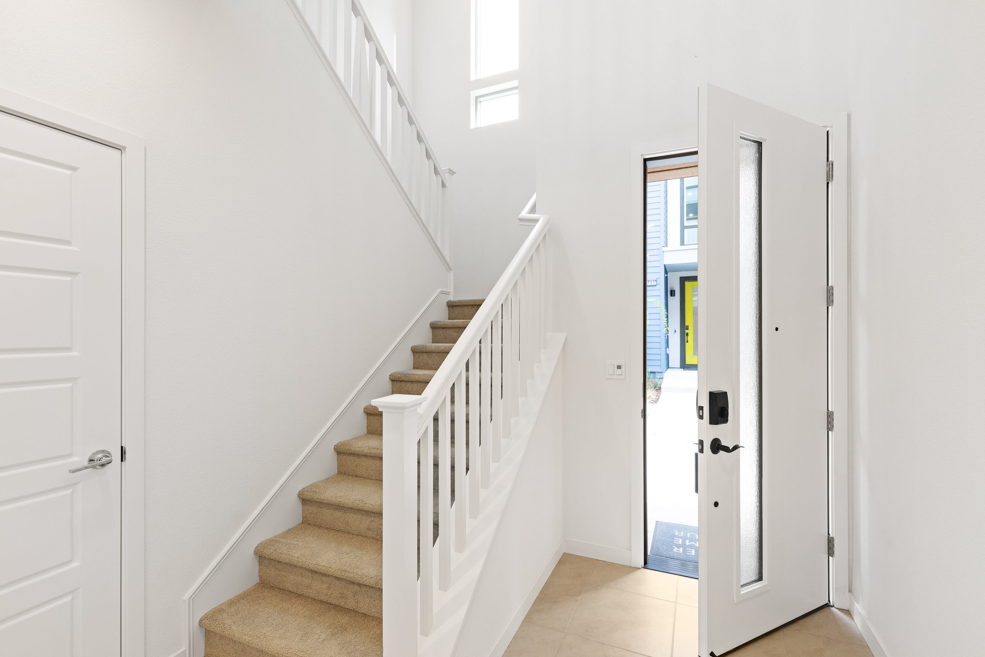 A bright and airy staircase leading up to a white door, with a minimalist and modern design aesthetic.