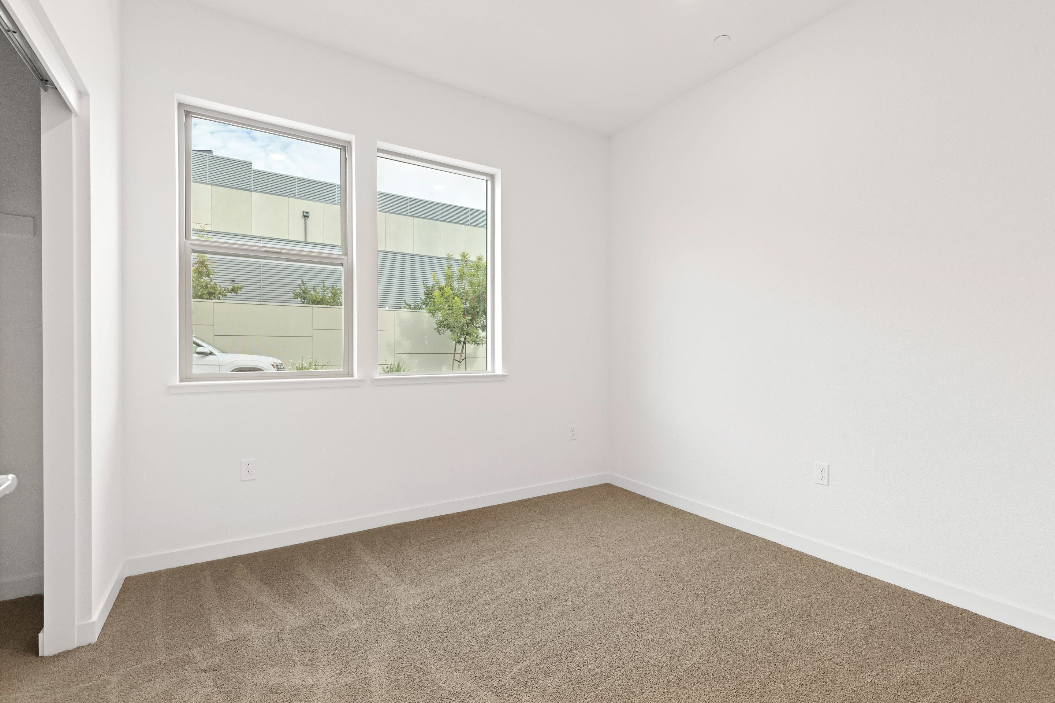 A bright, minimalist room with large windows overlooking a greenery-filled outdoor space.