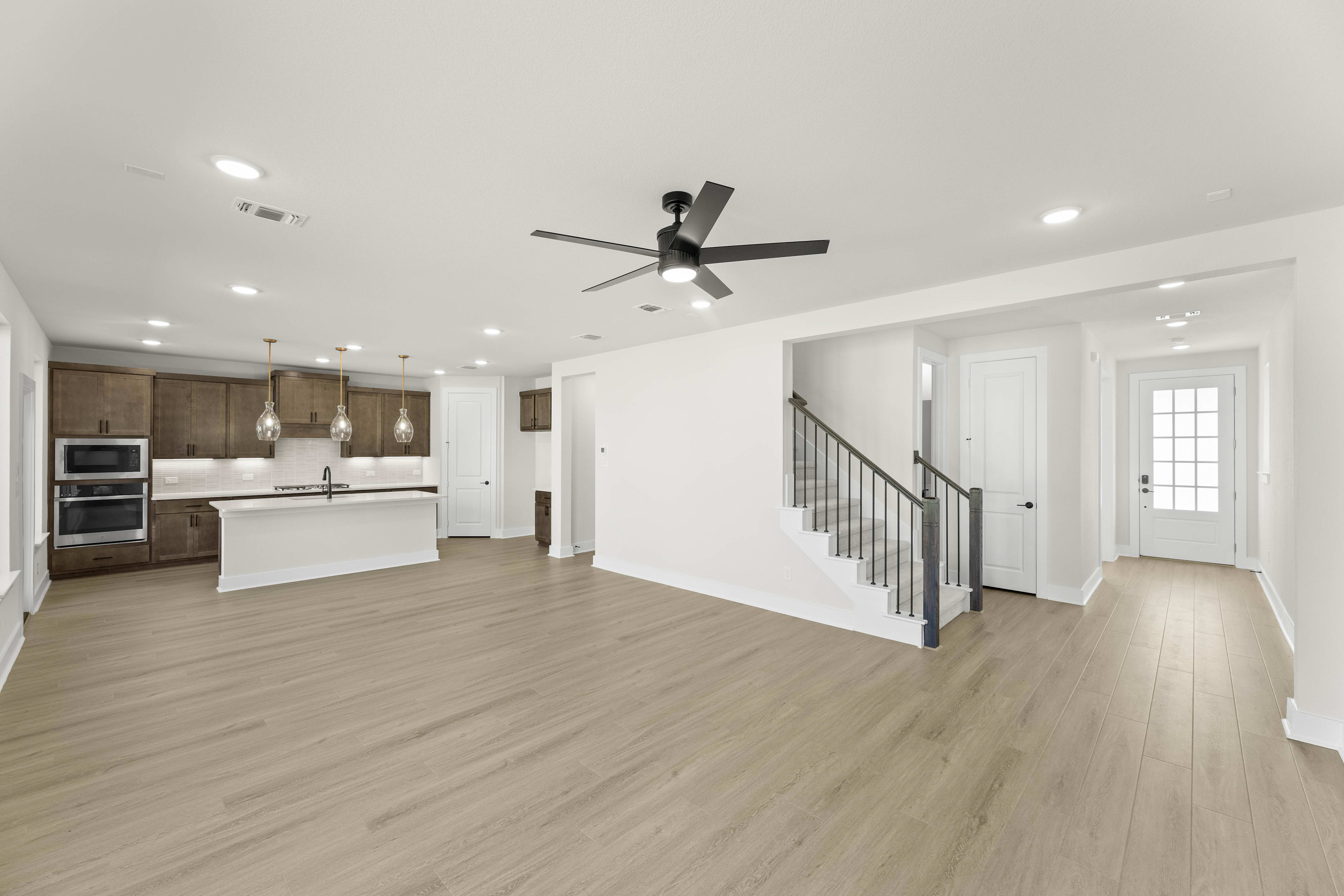 A modern, open-concept kitchen and living space with white walls, hardwood floors, and a ceiling fan.