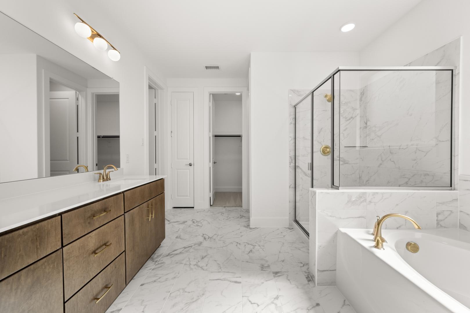 A spacious and modern bathroom with a marble-tiled floor, a wooden vanity with drawers, and a glass-enclosed shower area.