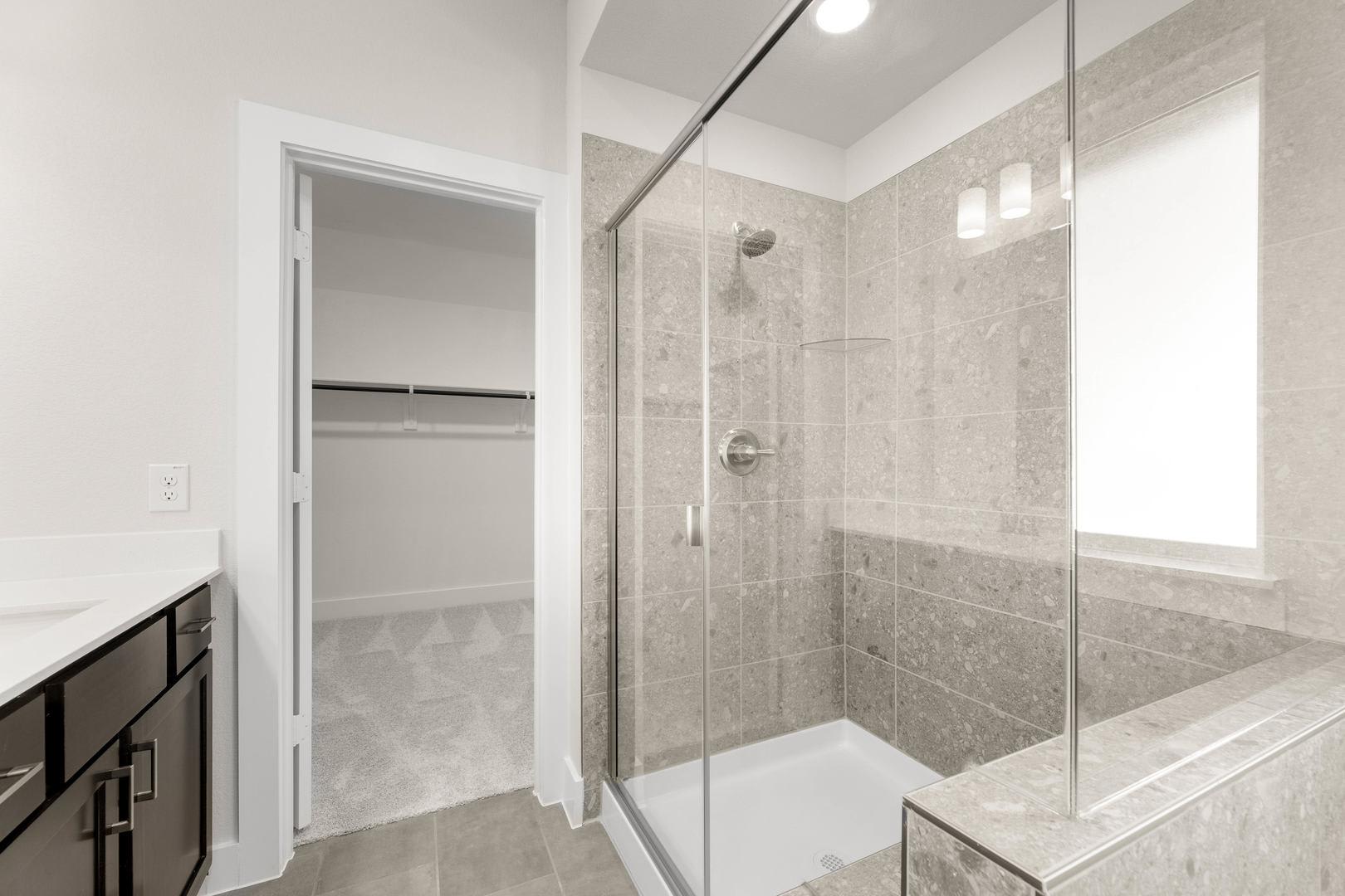 A modern, well-lit bathroom with a glass-enclosed shower, dark vanity cabinets, and a tiled floor and walls.