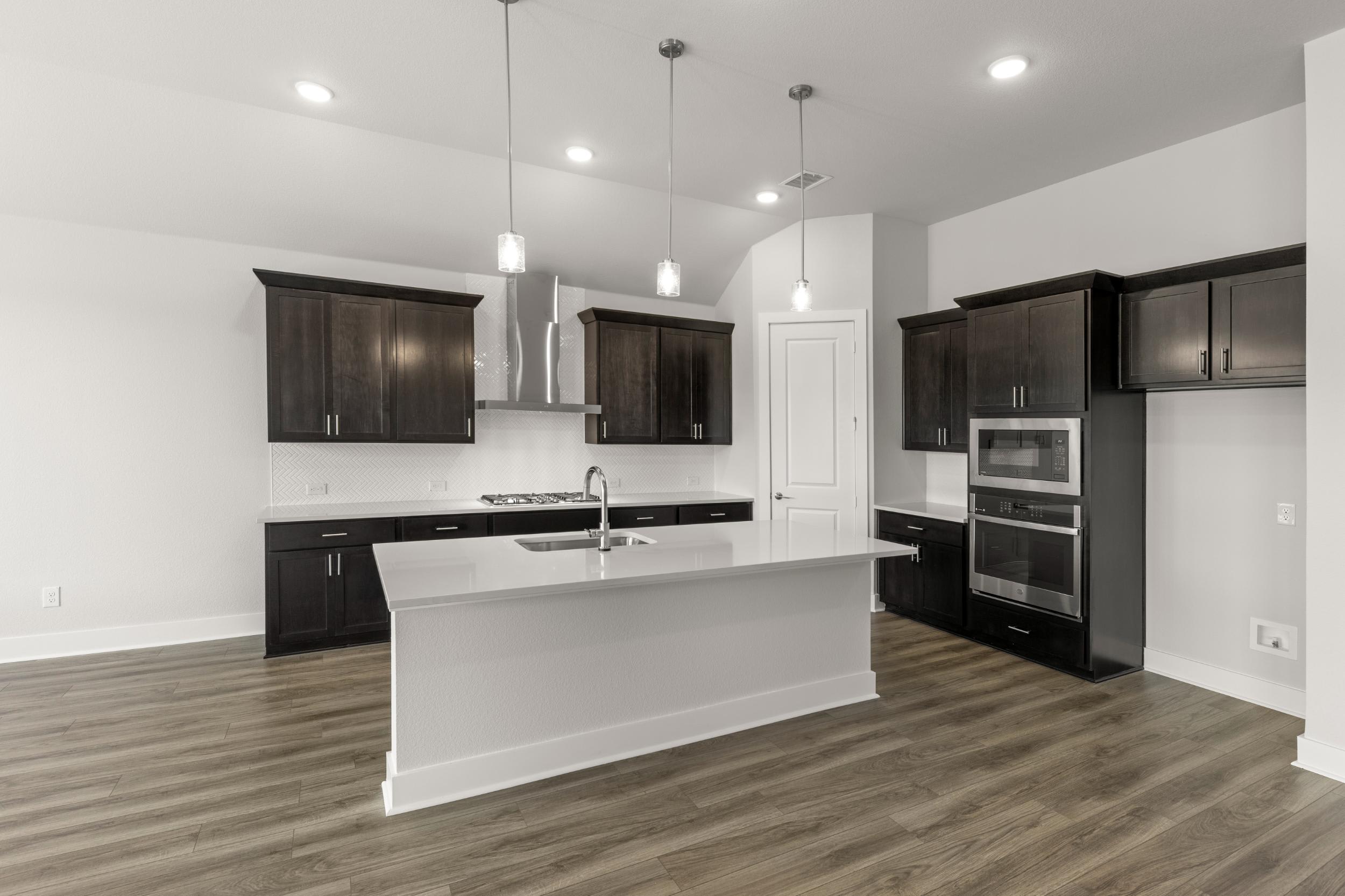 A modern, open-concept kitchen with dark wood cabinets, a white island, and hardwood flooring.