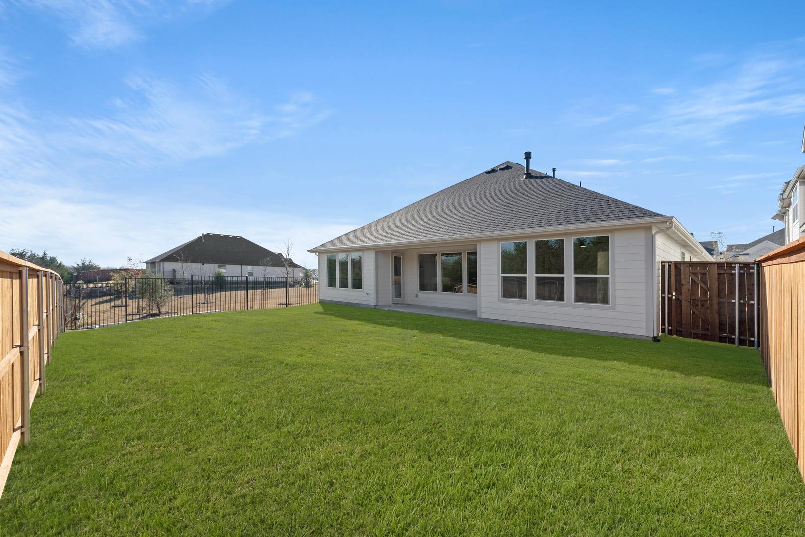 A well-manicured lawn surrounds a modern, single-story house with a peaked roof and large windows, set against a clear blue sky with wispy clouds.