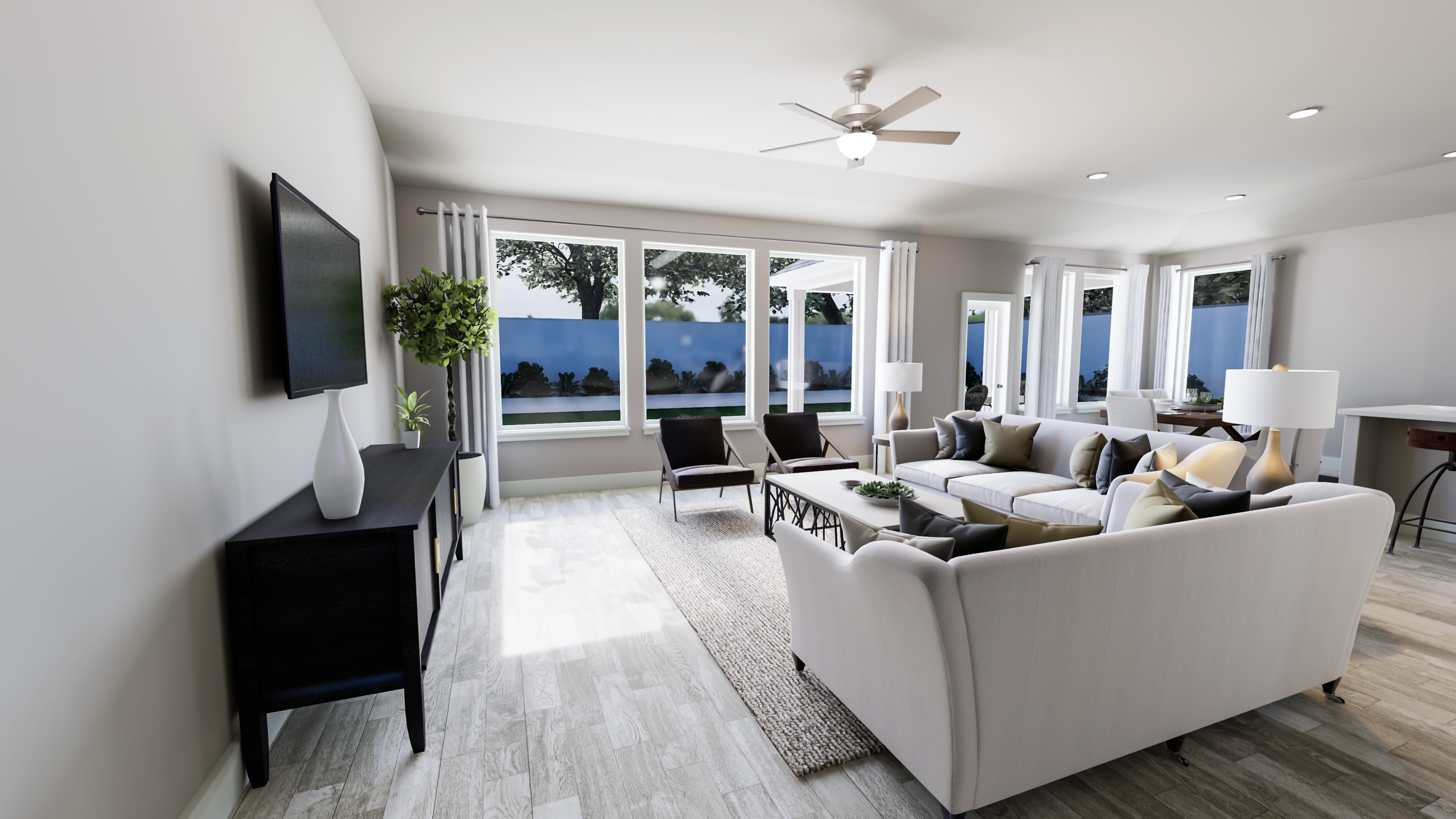 A modern and spacious living room with large windows overlooking a scenic outdoor view, featuring a comfortable seating arrangement, a ceiling fan, and a television mounted on the wall.