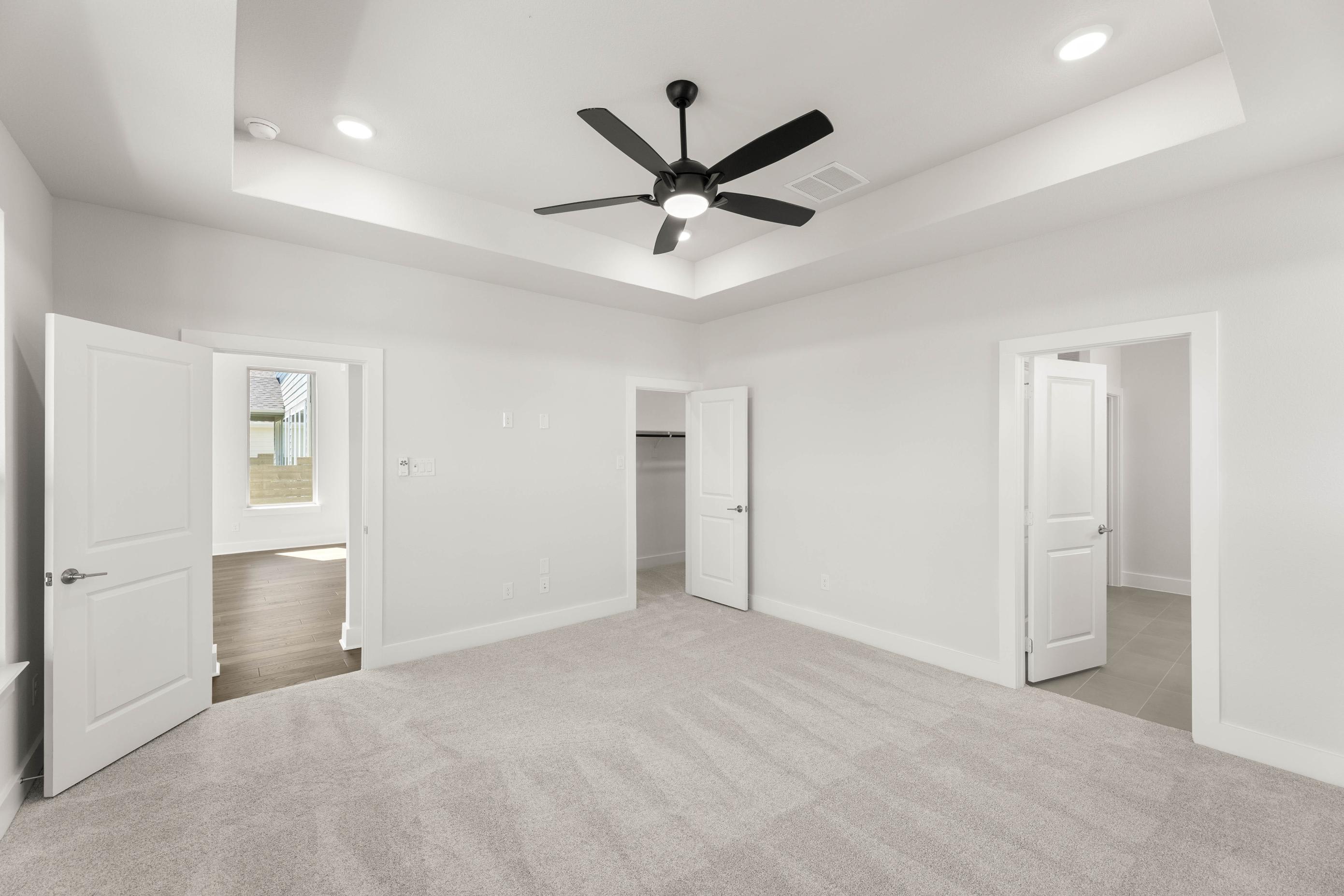 A spacious, minimalist room with white walls, a ceiling fan, and multiple doorways leading to other areas of the space.