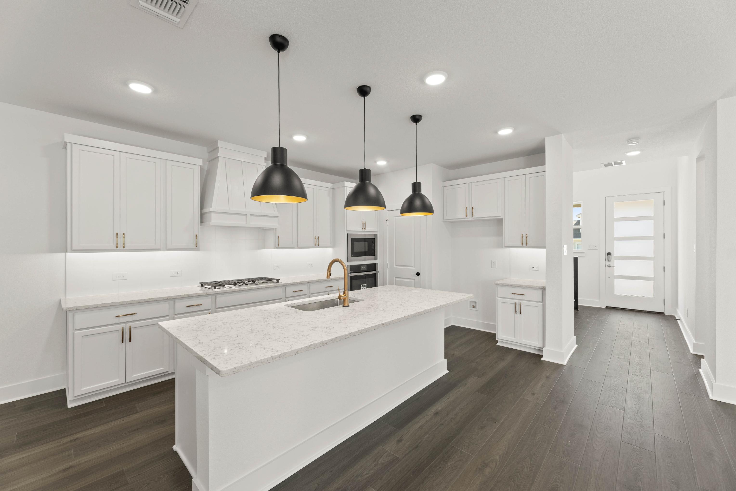 A modern, minimalist kitchen with white cabinets, a large island, and pendant lights hanging from the ceiling, set against a hardwood floor.