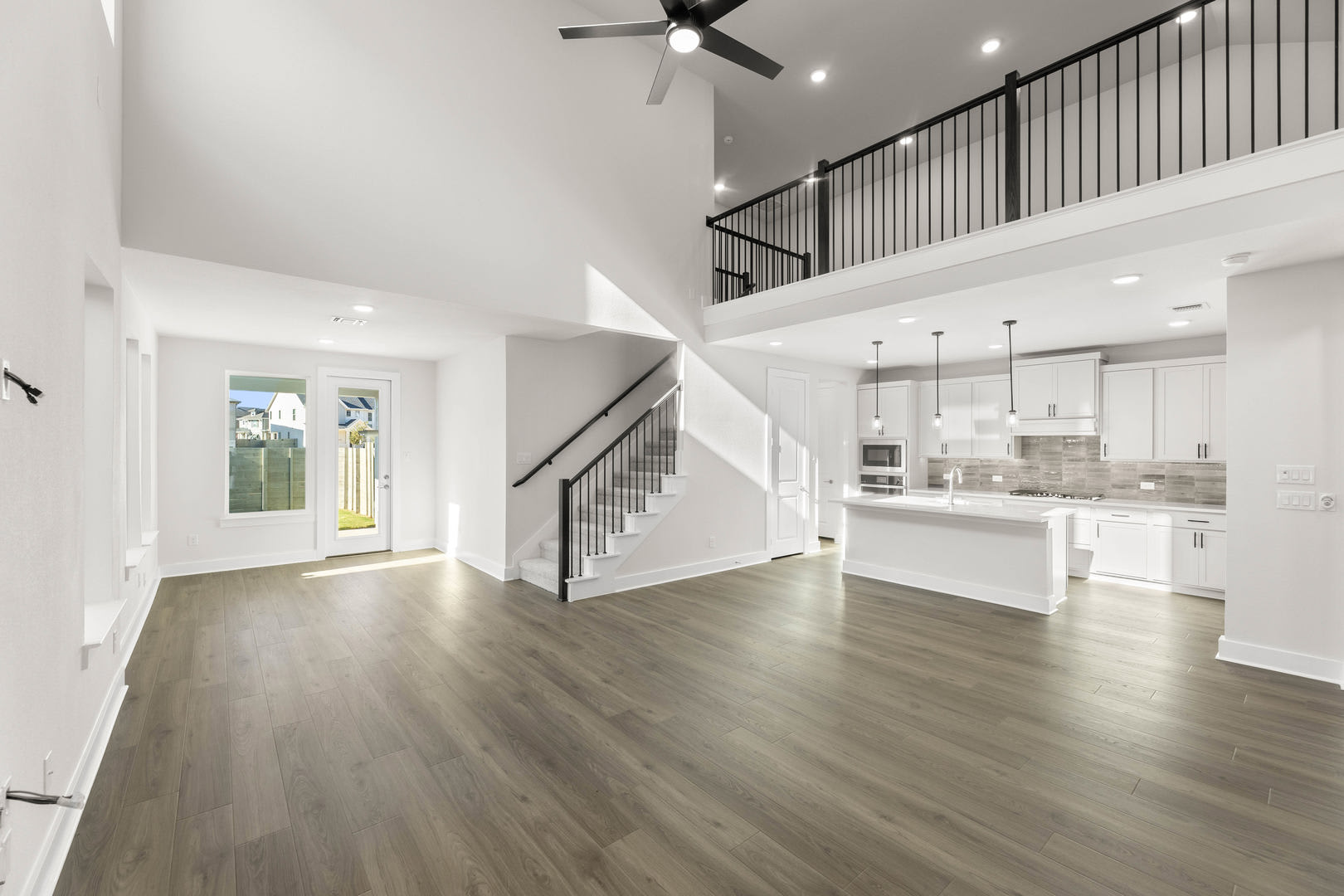 A spacious and modern open-concept living space with a kitchen, dining area, and staircase leading to an upper level, featuring hardwood floors, white walls, and contemporary lighting fixtures.