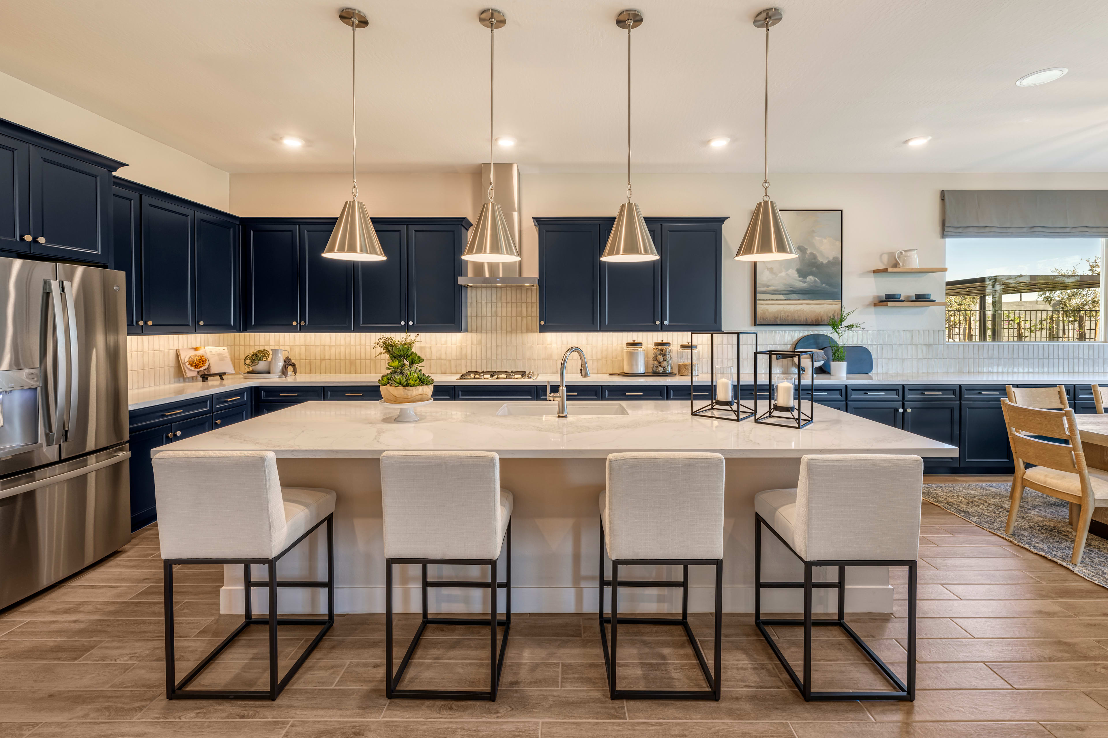 A modern and stylish kitchen with dark cabinets, a large island with bar stools, and pendant lights hanging above, set against a bright and airy background.
