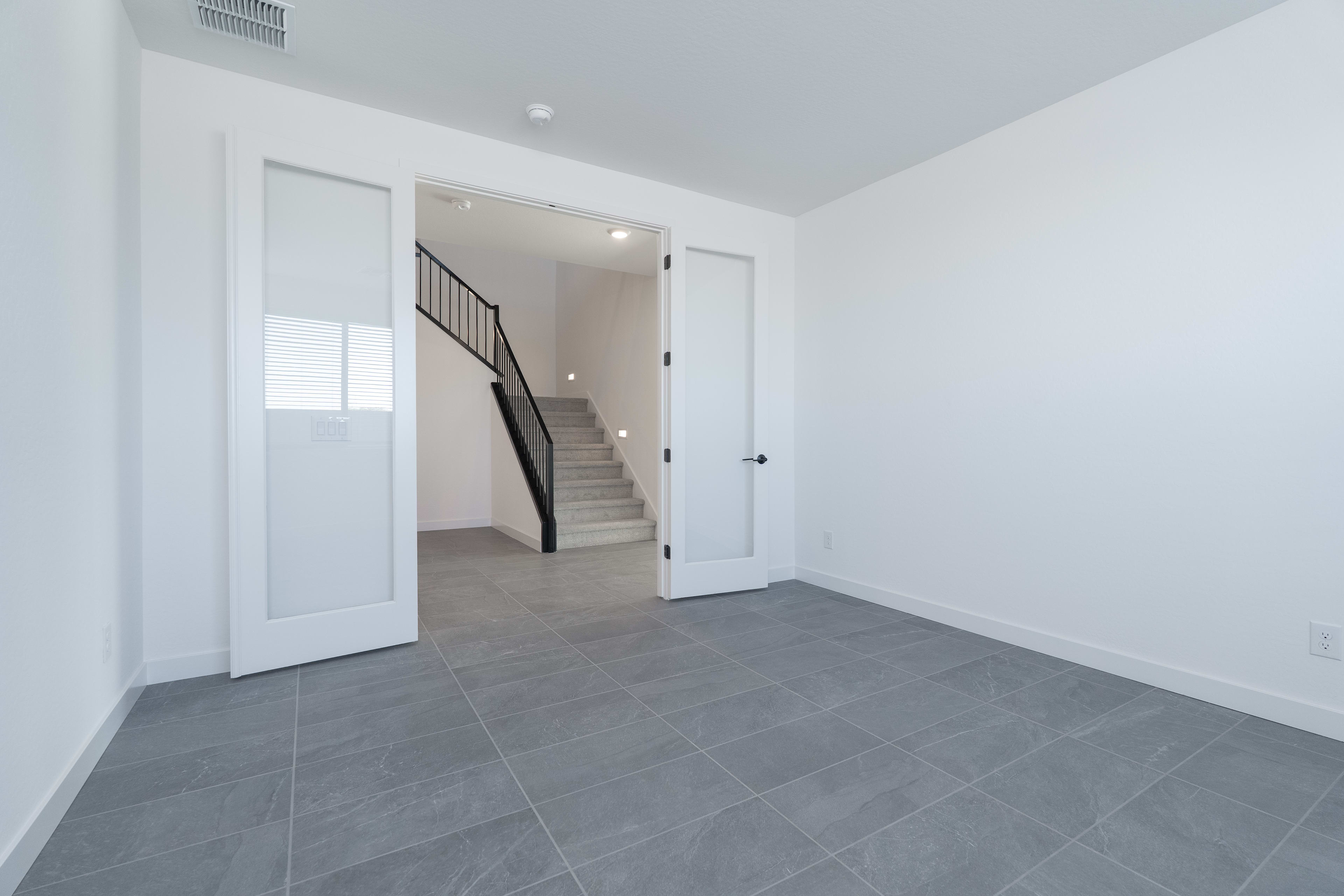 A spacious, minimalist entryway with white walls, a tiled gray floor, and a staircase leading to the upper level.