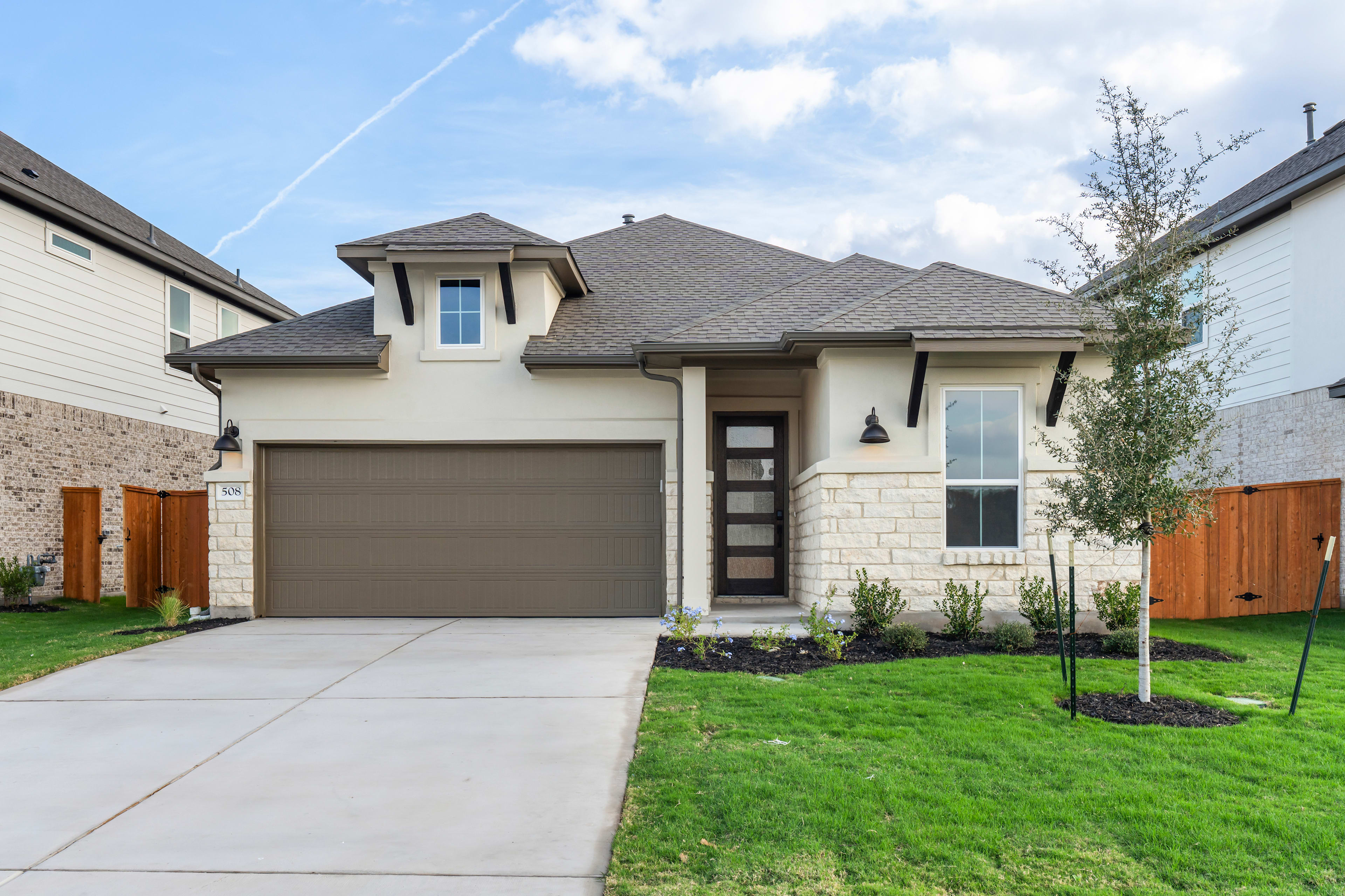 A two-story house with a garage, surrounded by a well-manicured lawn and landscaping, set against a cloudy blue sky.
